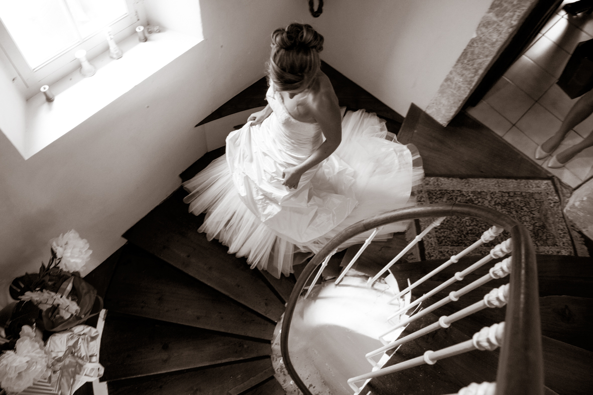 A woman in a wedding dress sitting on a spiral staircase viewed from above.