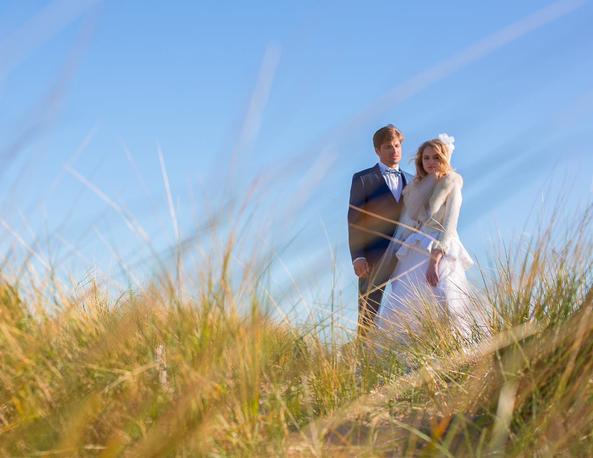 Jeune couple en vêtements de mariage dans un champ de hautes herbes sous un ciel bleu clair
