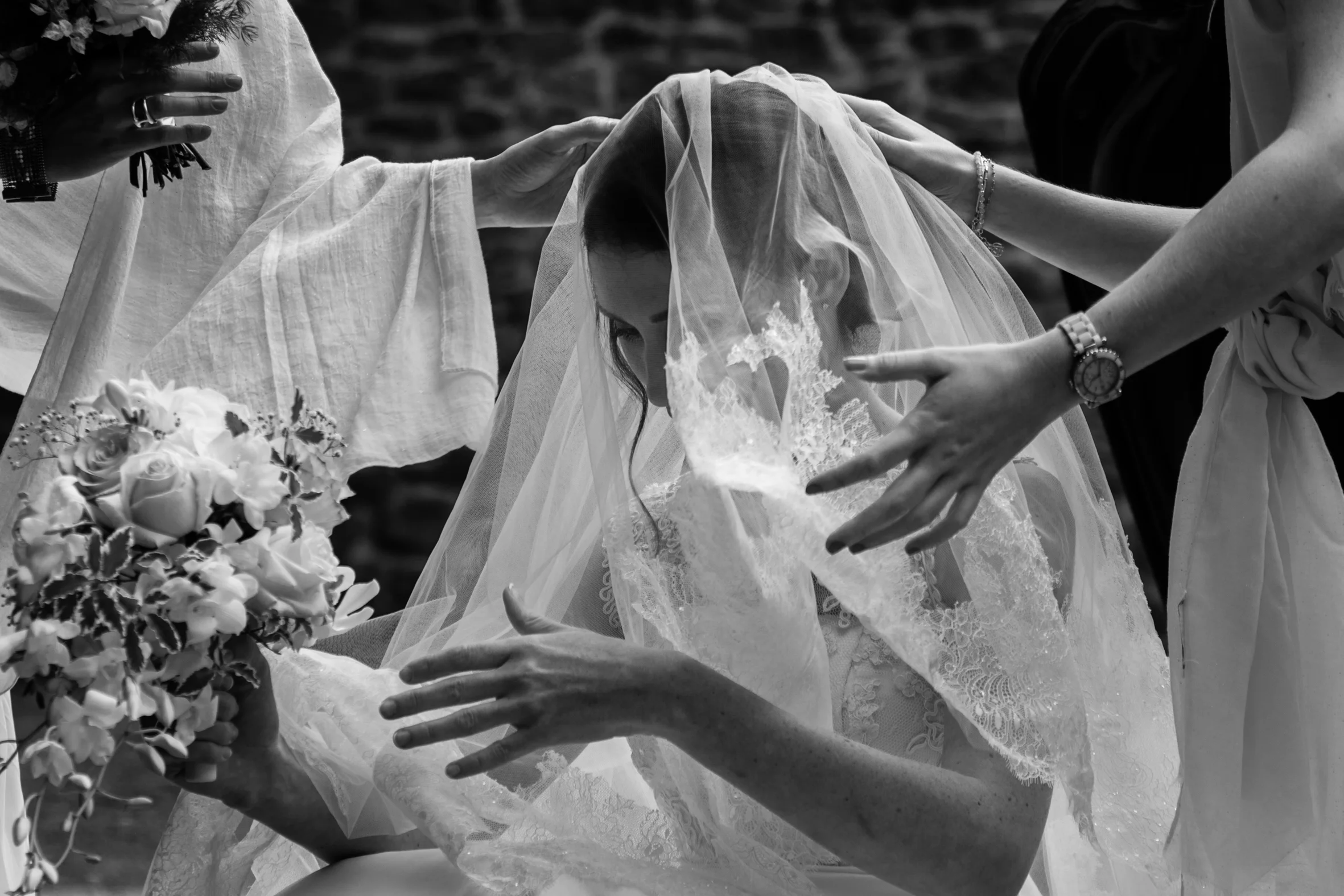 A bride with a veil is being assisted by women with flowers, during a wedding ceremony.