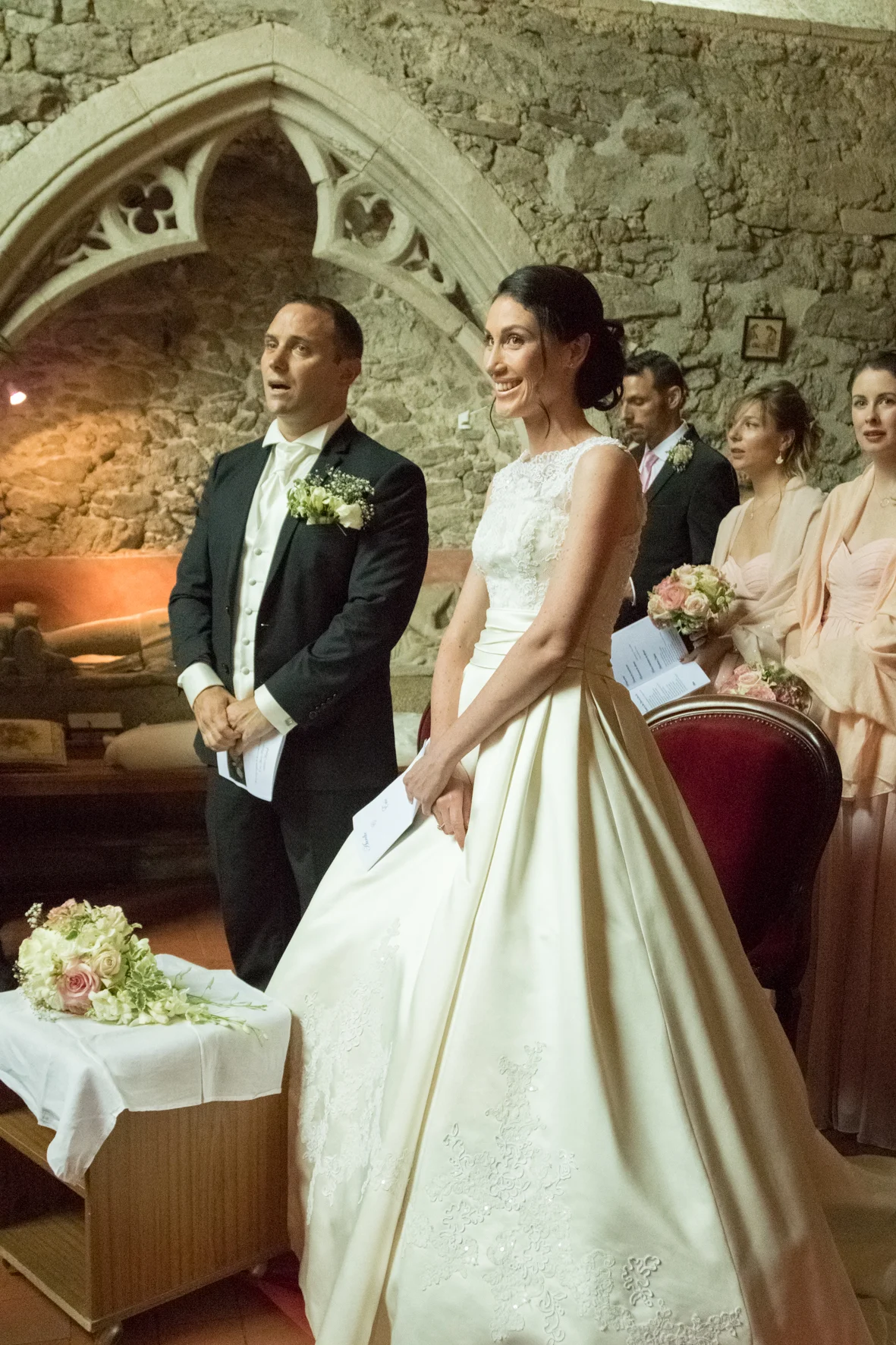 Cérémonie de mariage dans une vieille église en pierre, avec le couple marié et des témoins, toutes personnes en tenue de mariage, dans une ambiance chaleureuse.