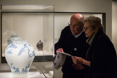   Museum visitors examine an 18th century Korean vase depicting a tiger smoking a long pipe, described by Miriam Mills, museum storyteller. May 2014.  