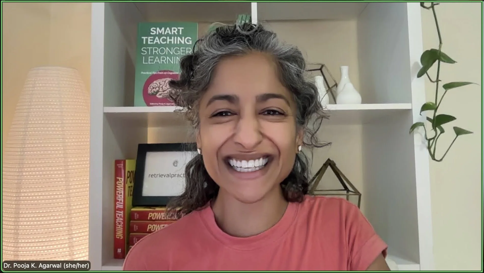 Woman in a pink shirt smiles in a Zoom video window.