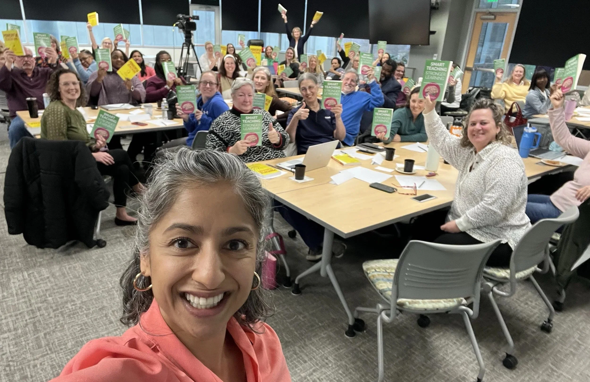 Selfie of Dr. Agarwal in a room with 40 educators holding up her two books