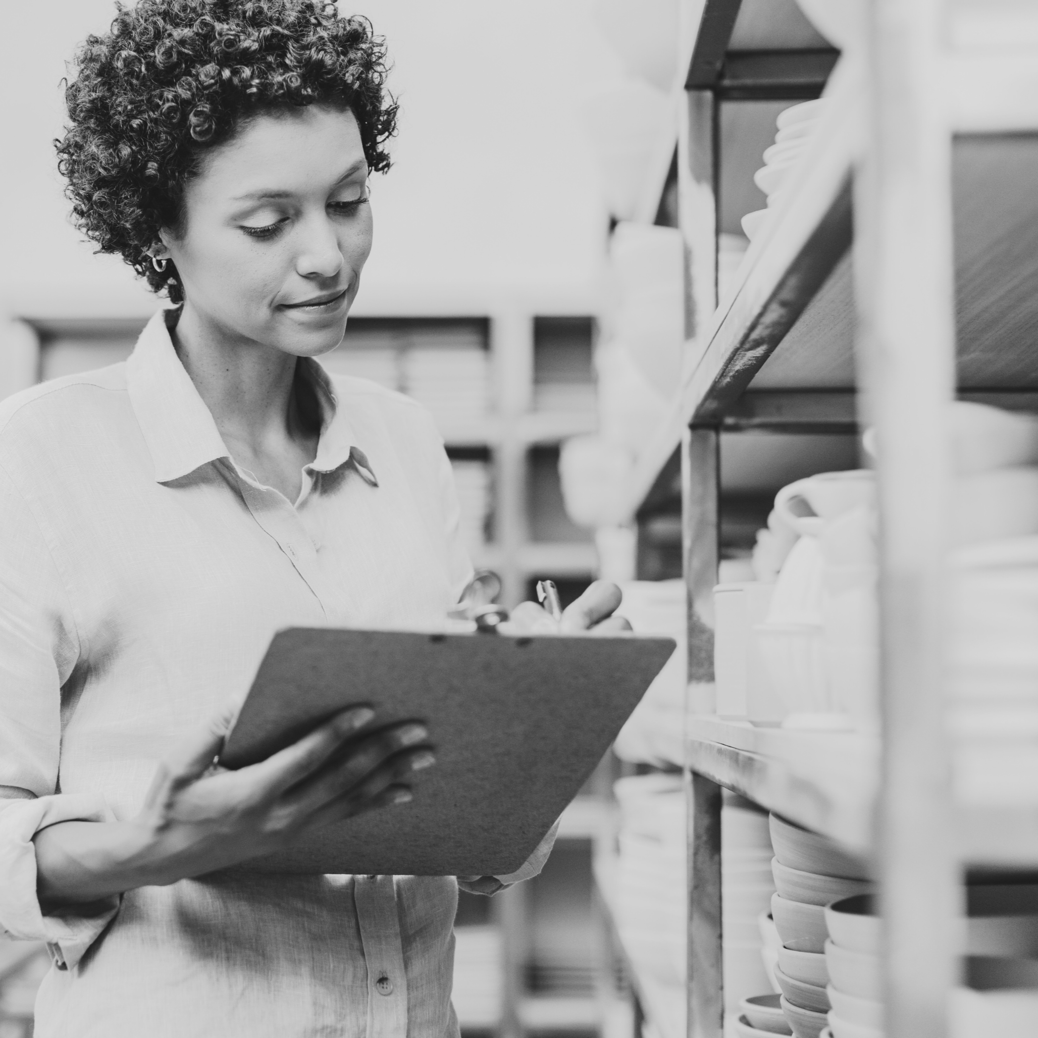 woman with curly dark hair takes inventory of shelf of handmade pottery