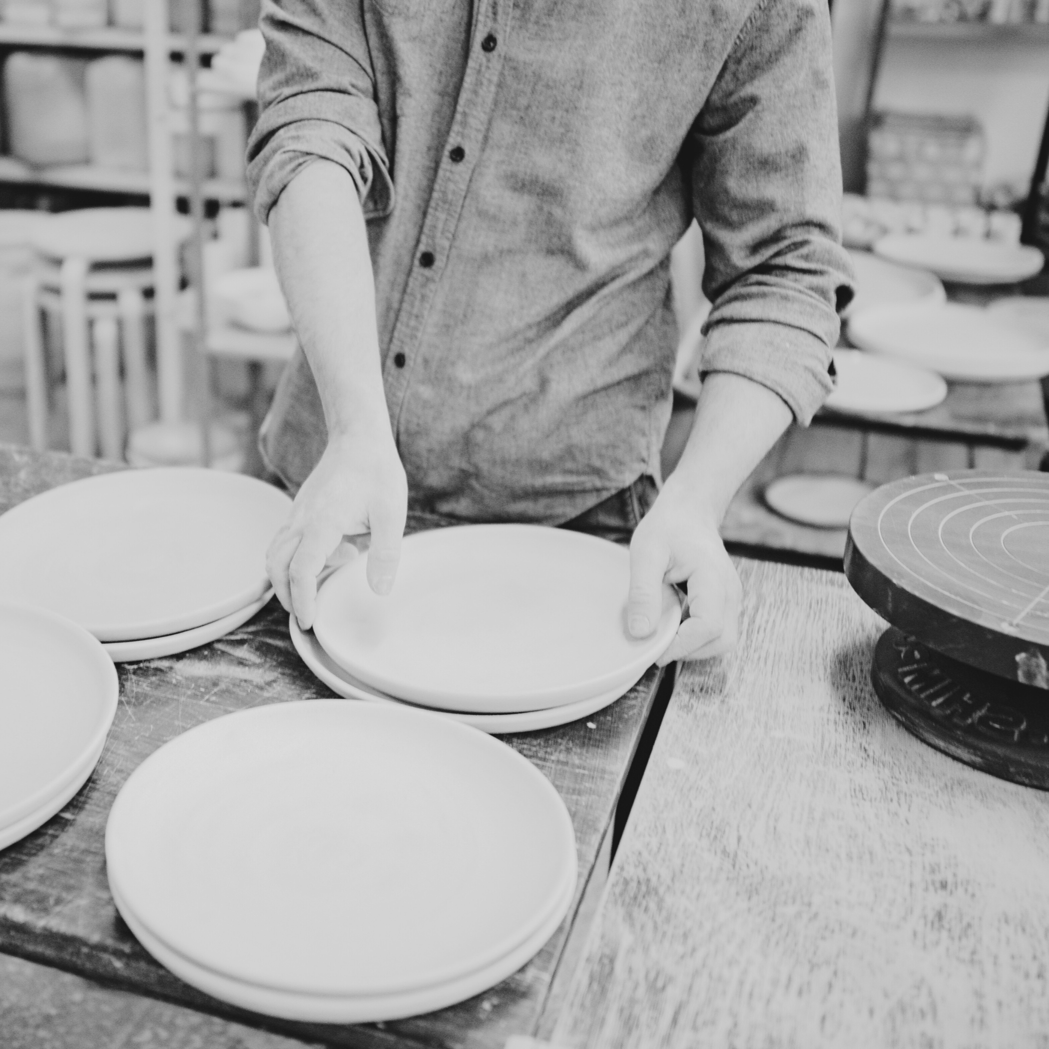 man in button down shirt stacks unglazed pottery plates in an artists studio
