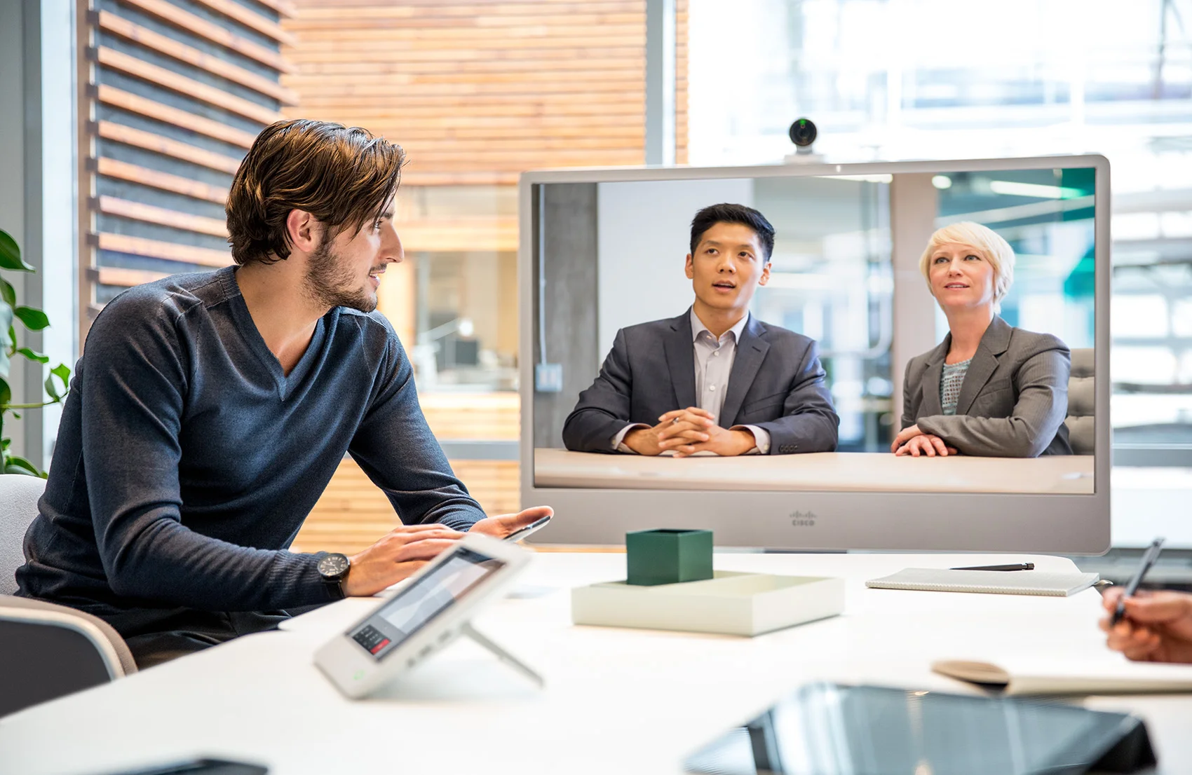 Man collaborating with ethnic male and executive woman using cisco telepresence in a modern building