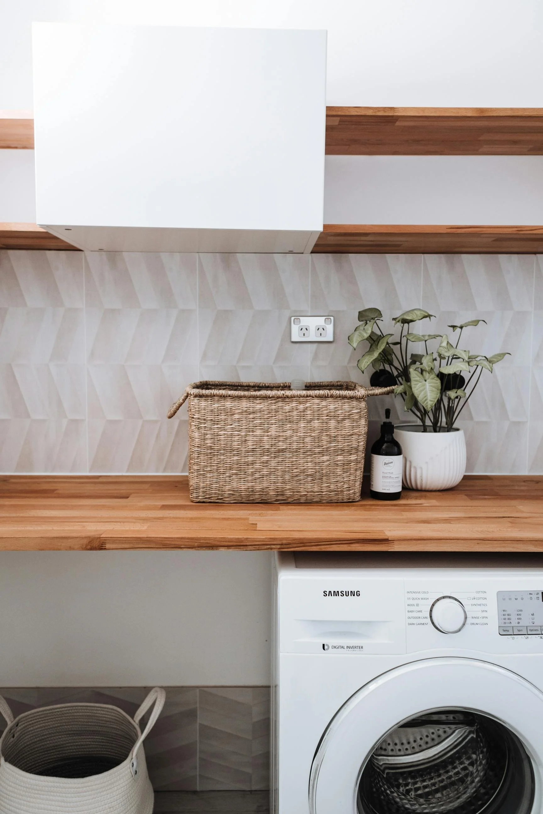 Clean laundry room with woven baskets, greenery, and organized appliances.