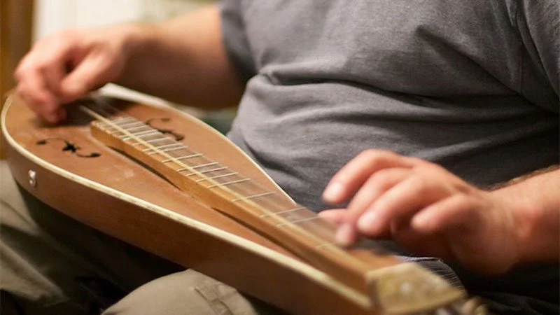 Close-up of person playing a mountain dulcimer.