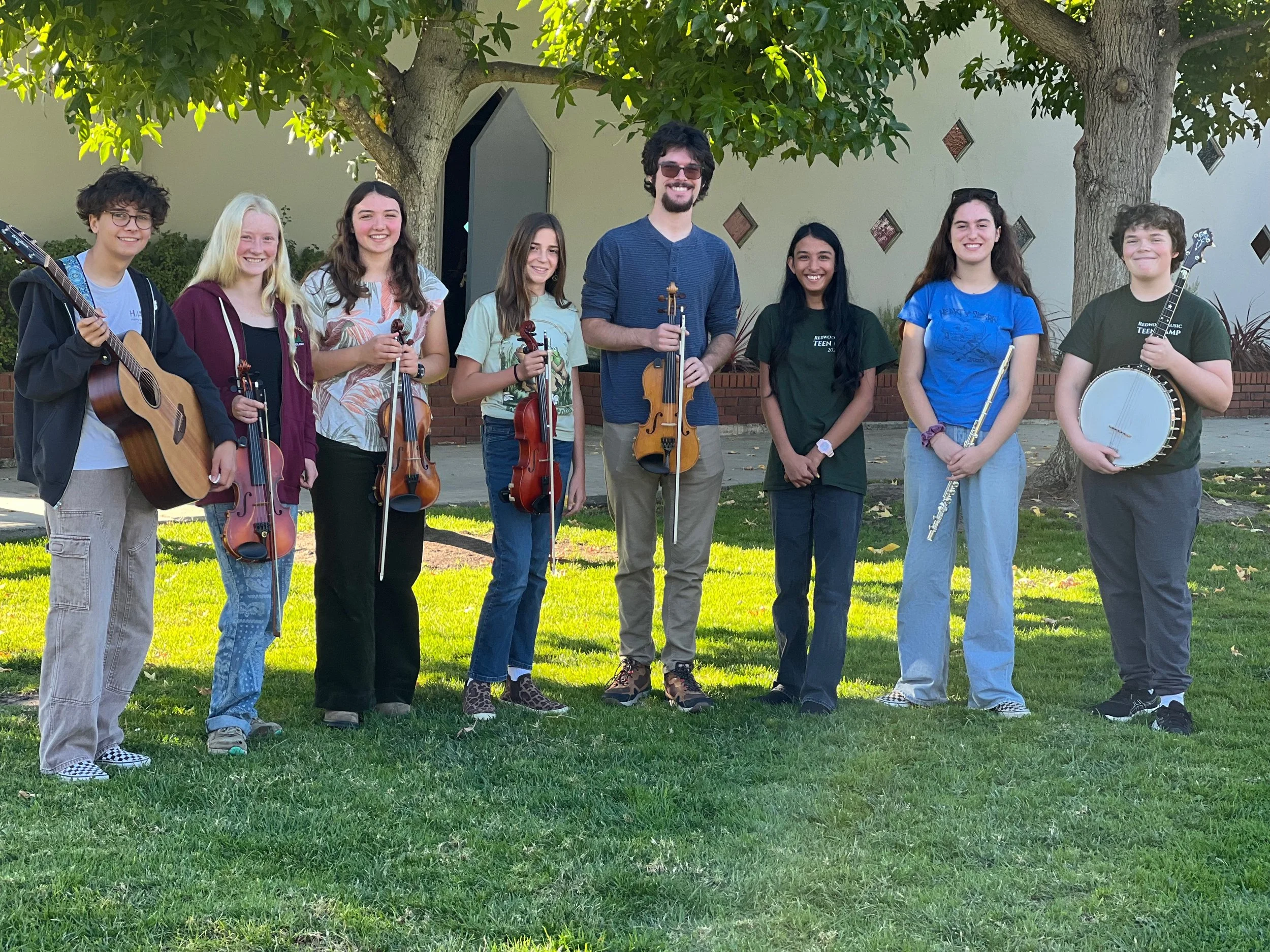 Seven smiling teenagers and the teacher hold their instruments in a group photo