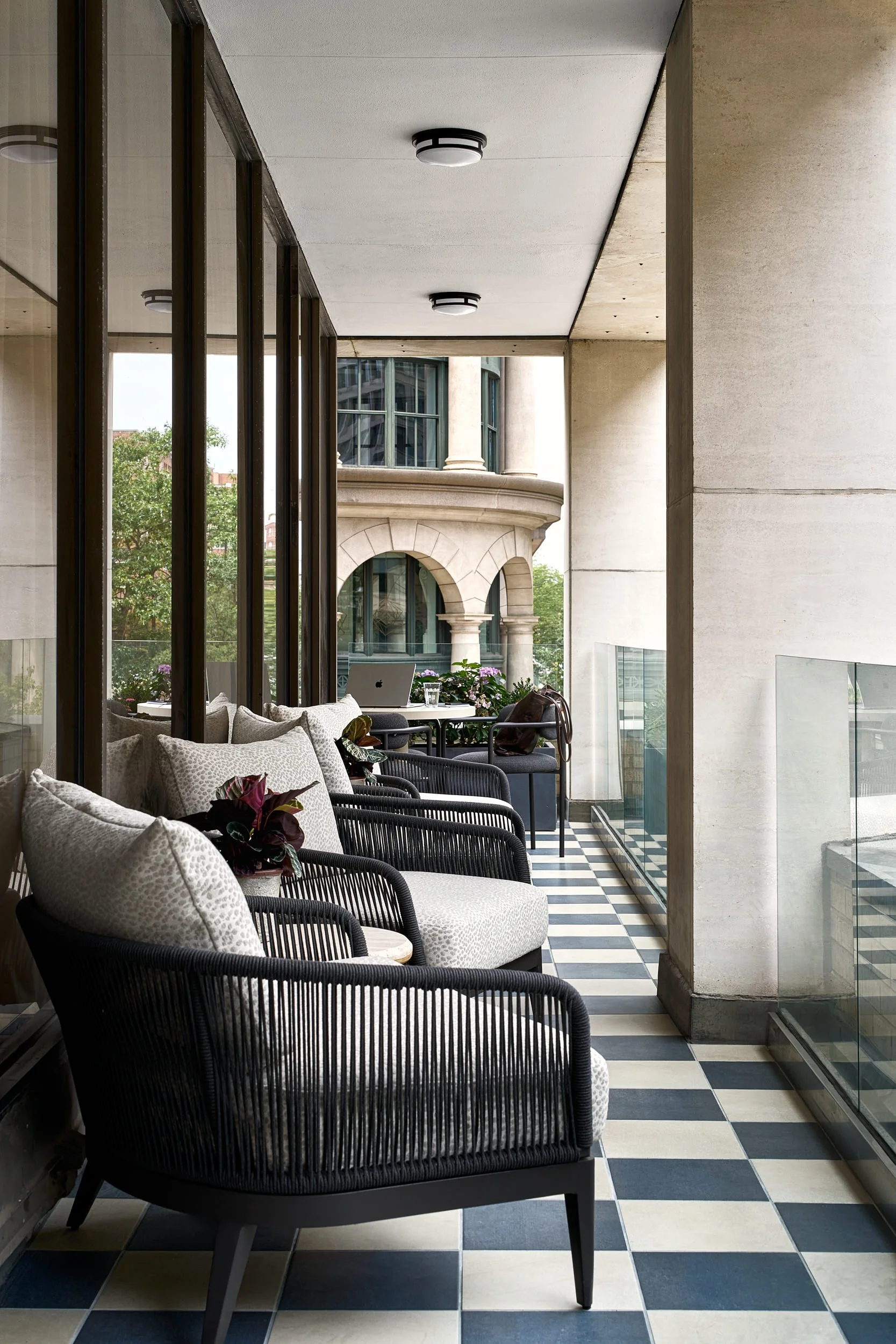 Outdoor balcony terrace lounge at The Malin DC with black rope lounge chairs and a checkered tile floor overlooking Washington, D.C. architecture.