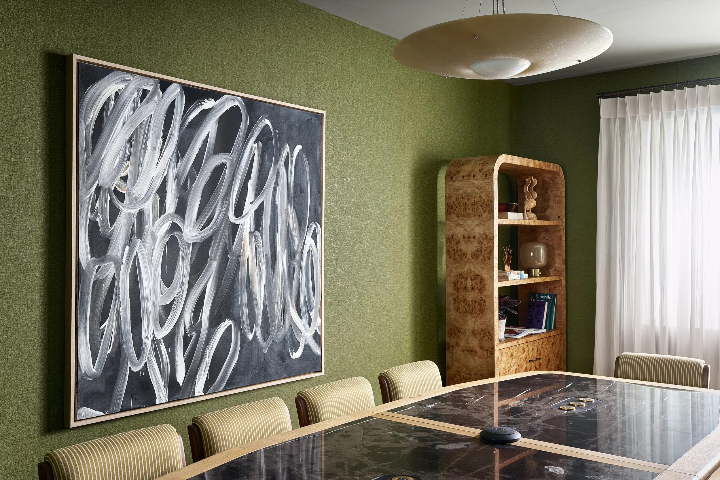Private conference room at The Malin DC featuring a large black and white abstract painting, striped upholstered seating, and a burl wood bookshelf.