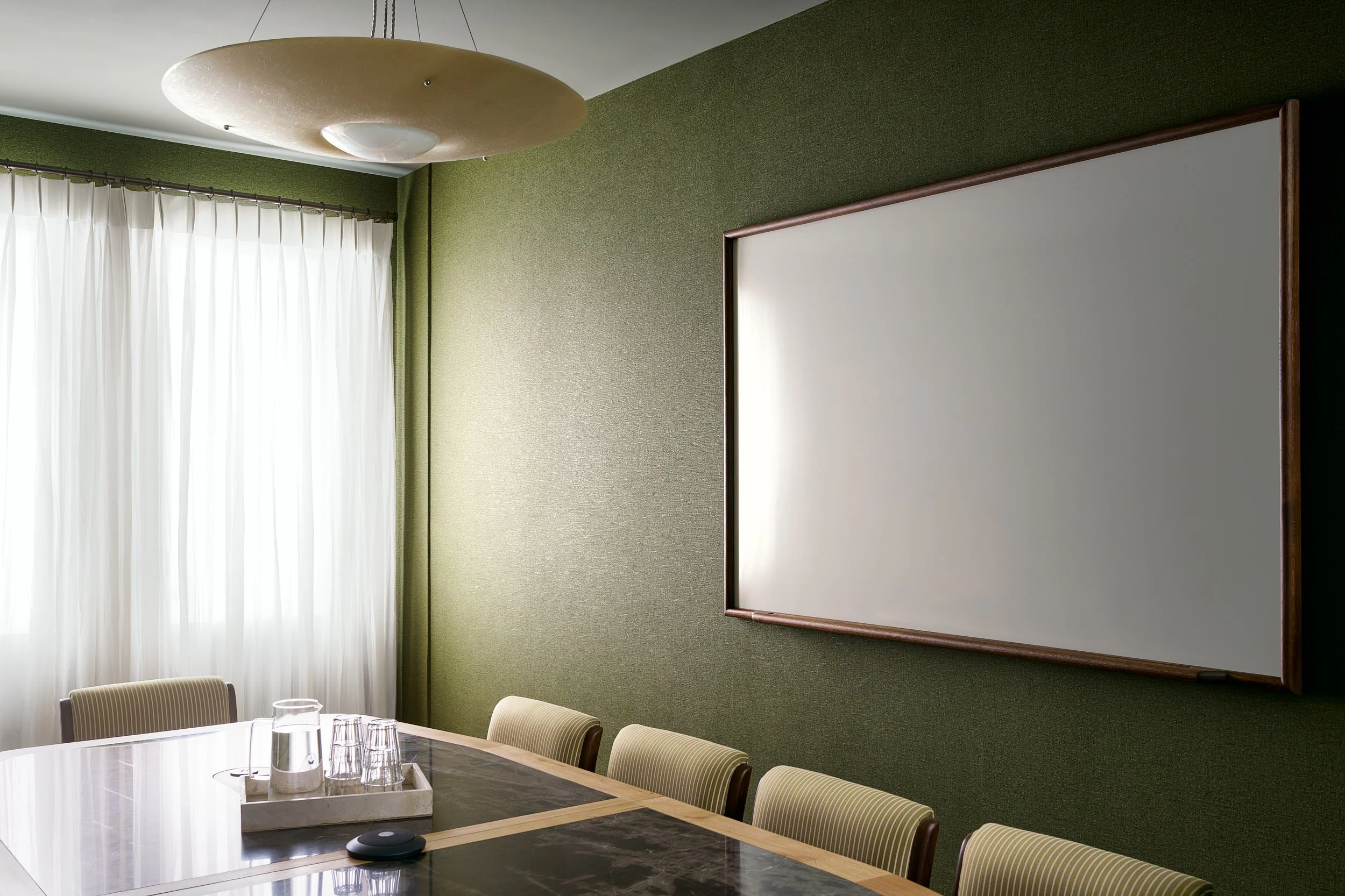 Conference room corner at The Malin DC with a large whiteboard, green textured wallpaper, and fabric seating.