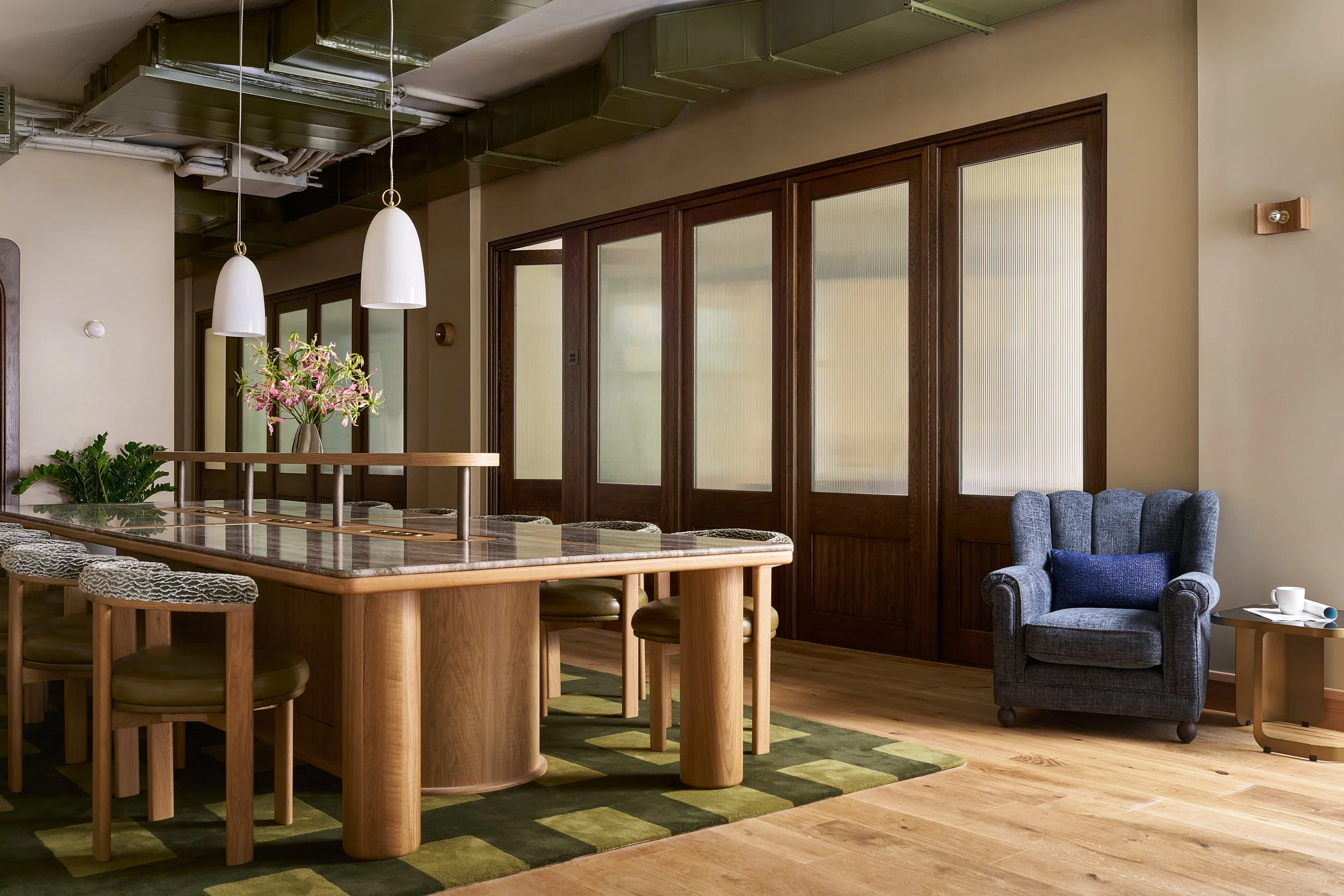 Bar-height communal coworking table at The Malin DC with glass-paneled French doors and a blue wingback armchair.