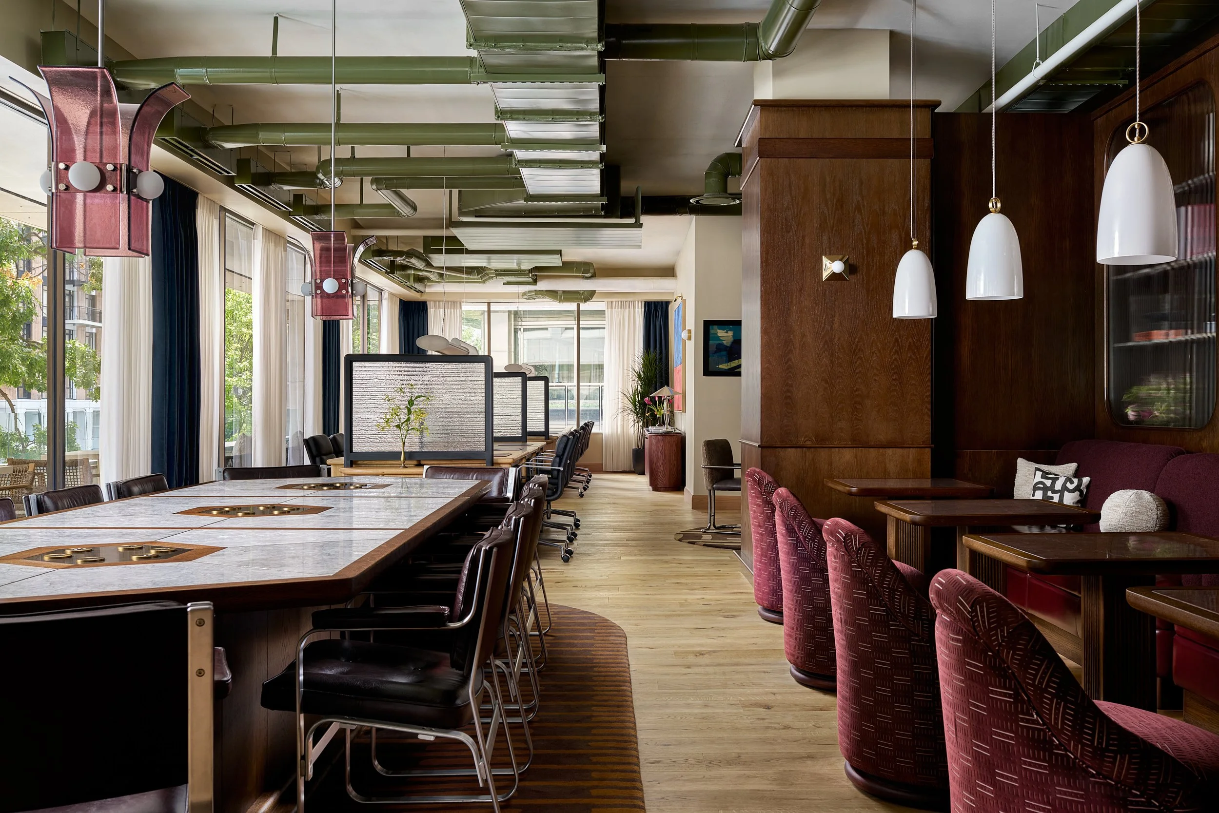 Coworking communal table at The Malin DC with pink glass pendant lights, burgundy leather chairs, and cafe seating.