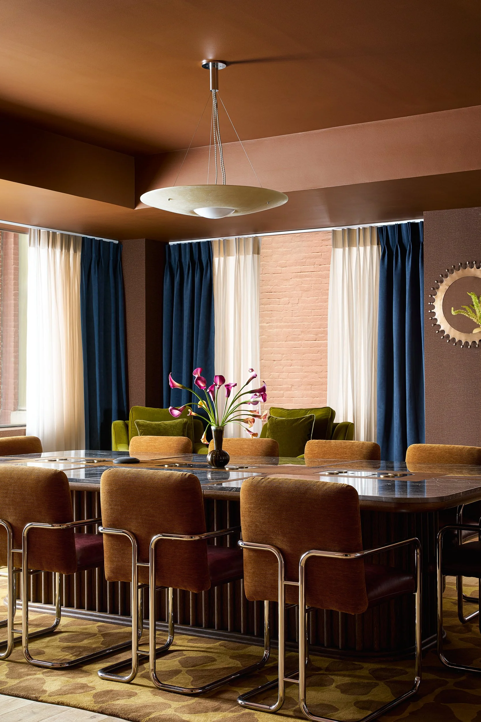 Coworking conference room at The Malin DC featuring a marble table, mustard velvet chairs, and an exposed brick accent wall.