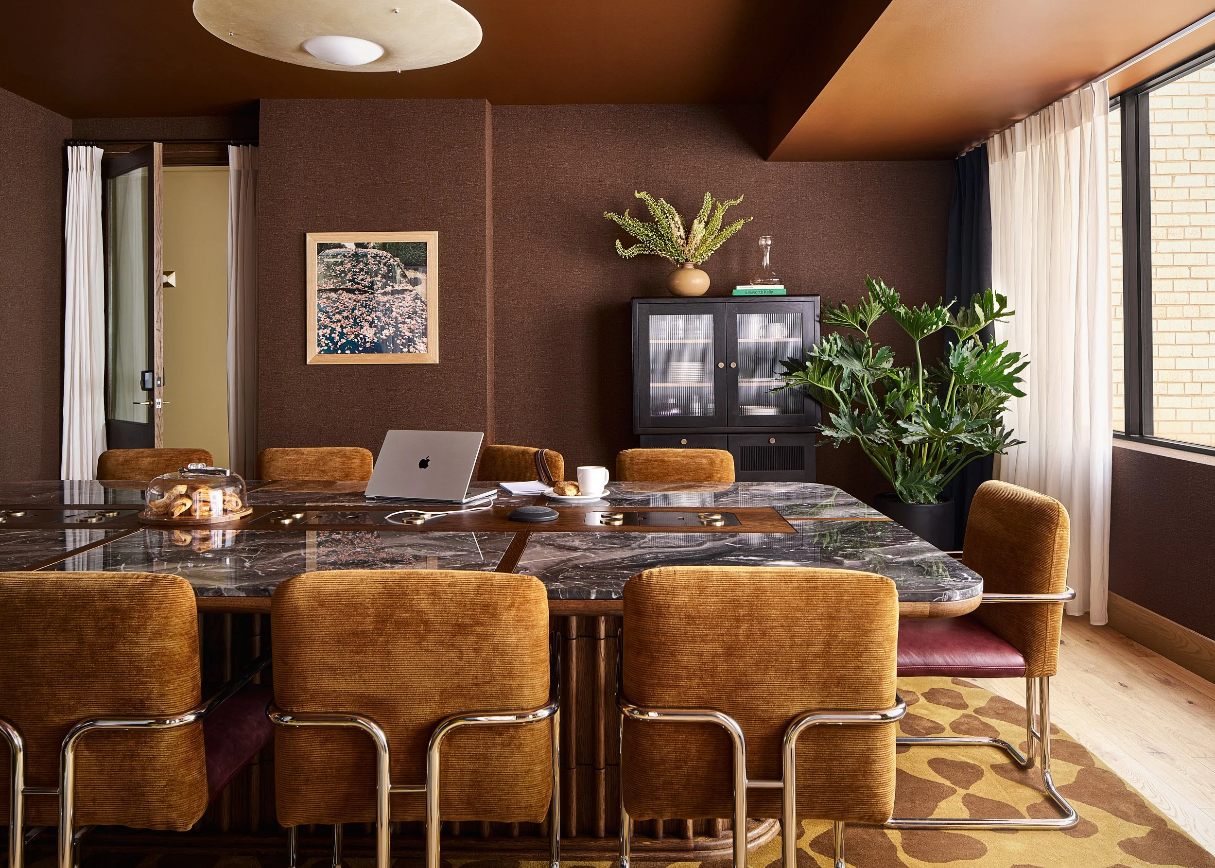 Coworking conference room at The Malin DC with a marble table, mustard velvet chairs, a glass-front china cabinet, and vibrant orange ceilings.