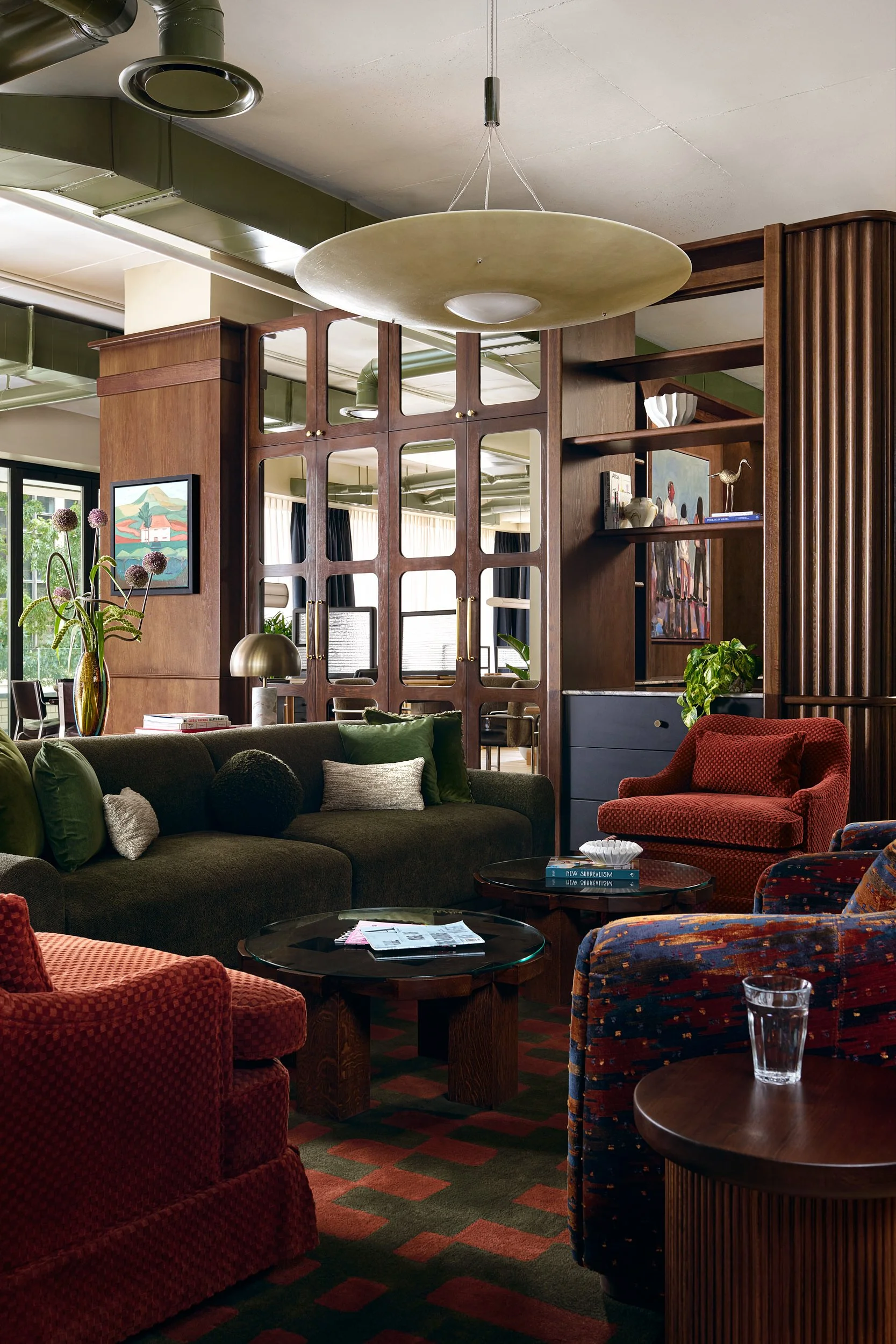 Coworking lounge at The Malin DC with an olive green sofa, red velvet armchairs, and mirrored cabinet doors.