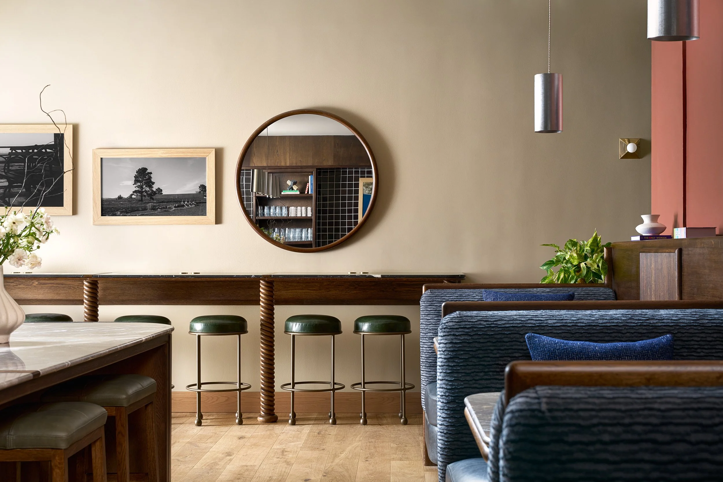 Bar-height dining and work tables at The Malin DC coworking space with a round wood mirror, green stools, and navy blue booth seating.