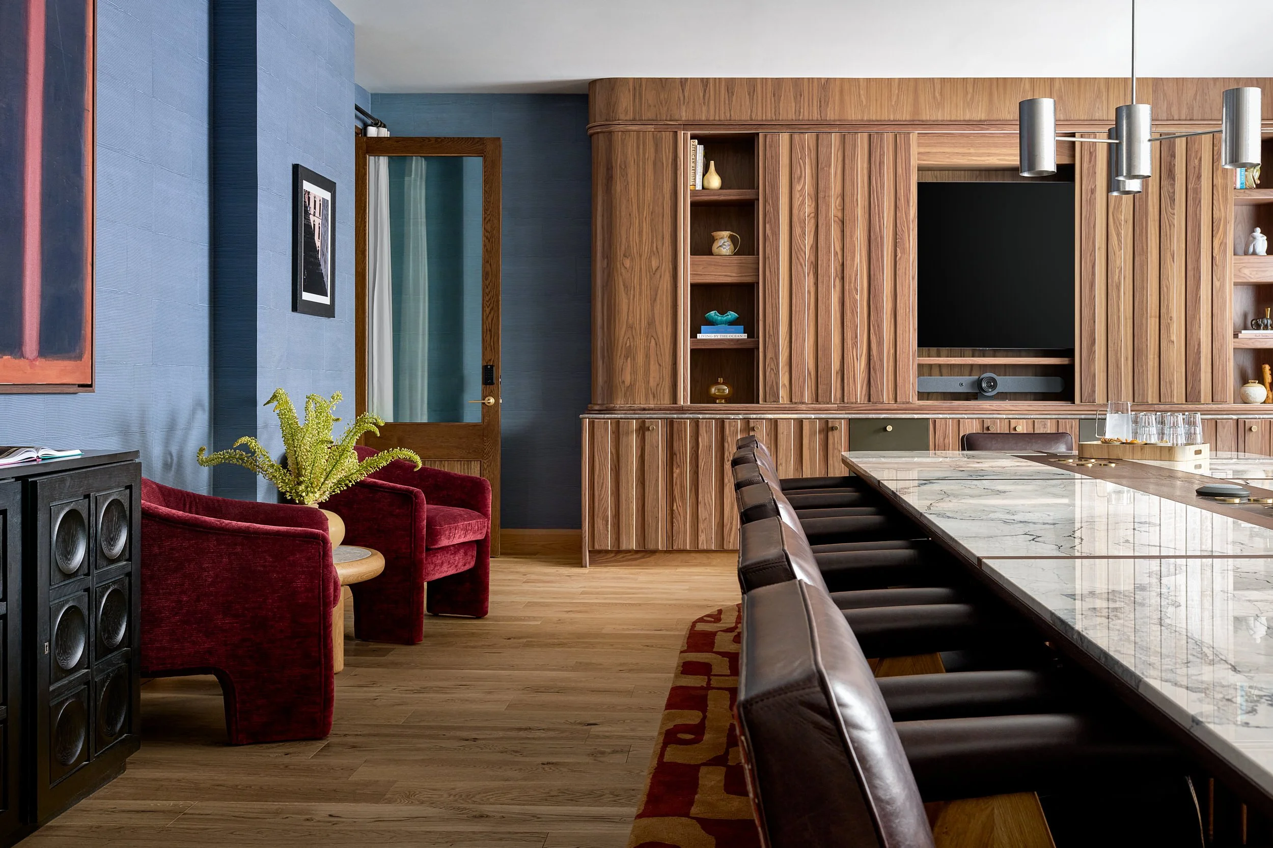 Lounge and media area at The Malin DC with a wood-paneled TV wall, burgundy velvet chairs, and blue wallpaper.