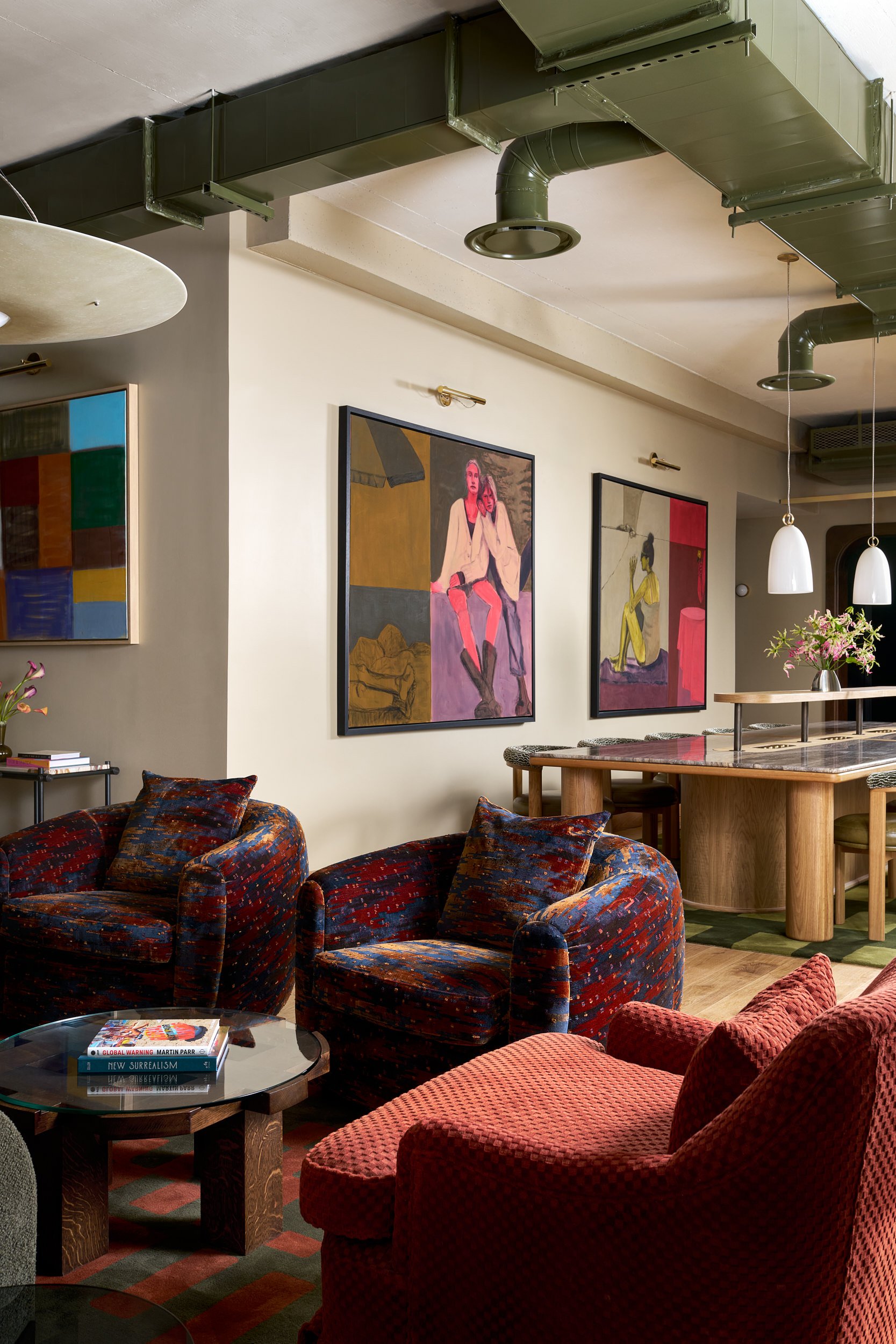 Lounge seating area at The Malin DC with red and blue patterned armchairs beneath colorful figurative paintings.
