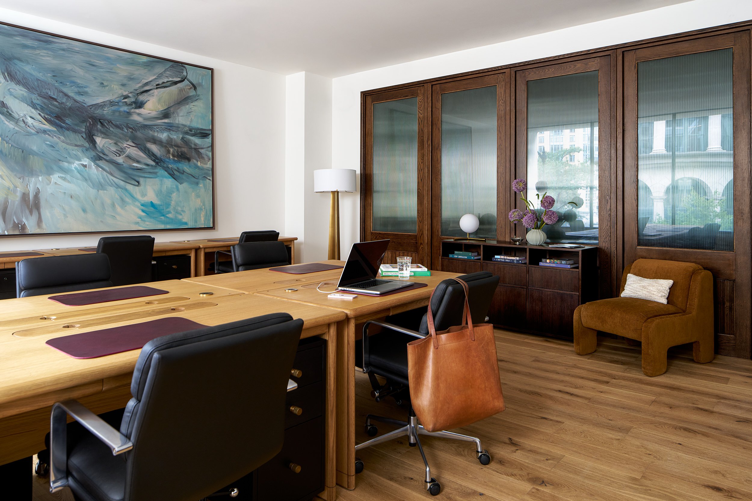 Private office at The Malin DC with shared wood desks and a large blue abstract painting on the wall.