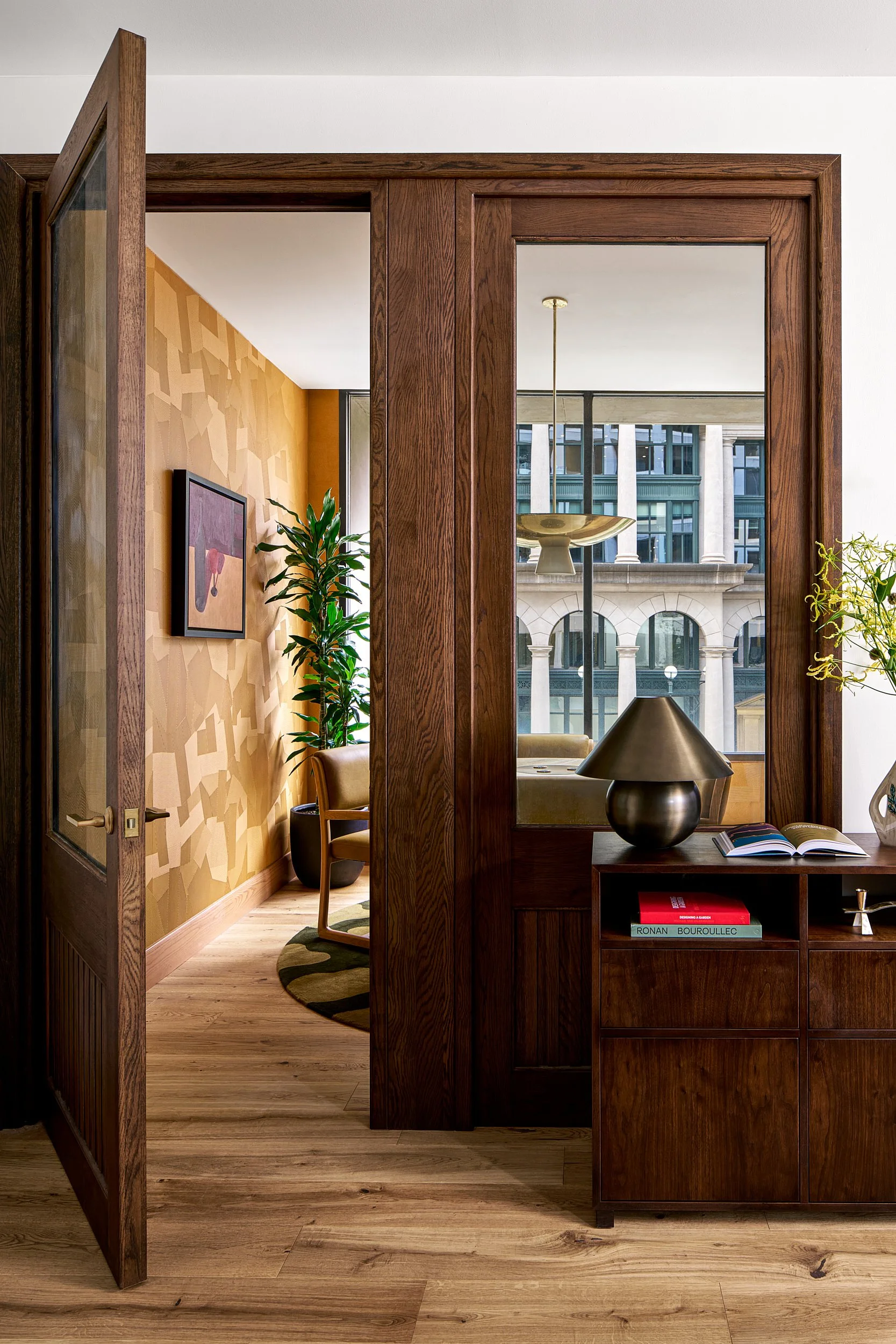 Entrance to a private office suite at The Malin DC through a glass and wood paneled door, with a city view reflected in the mirror.
