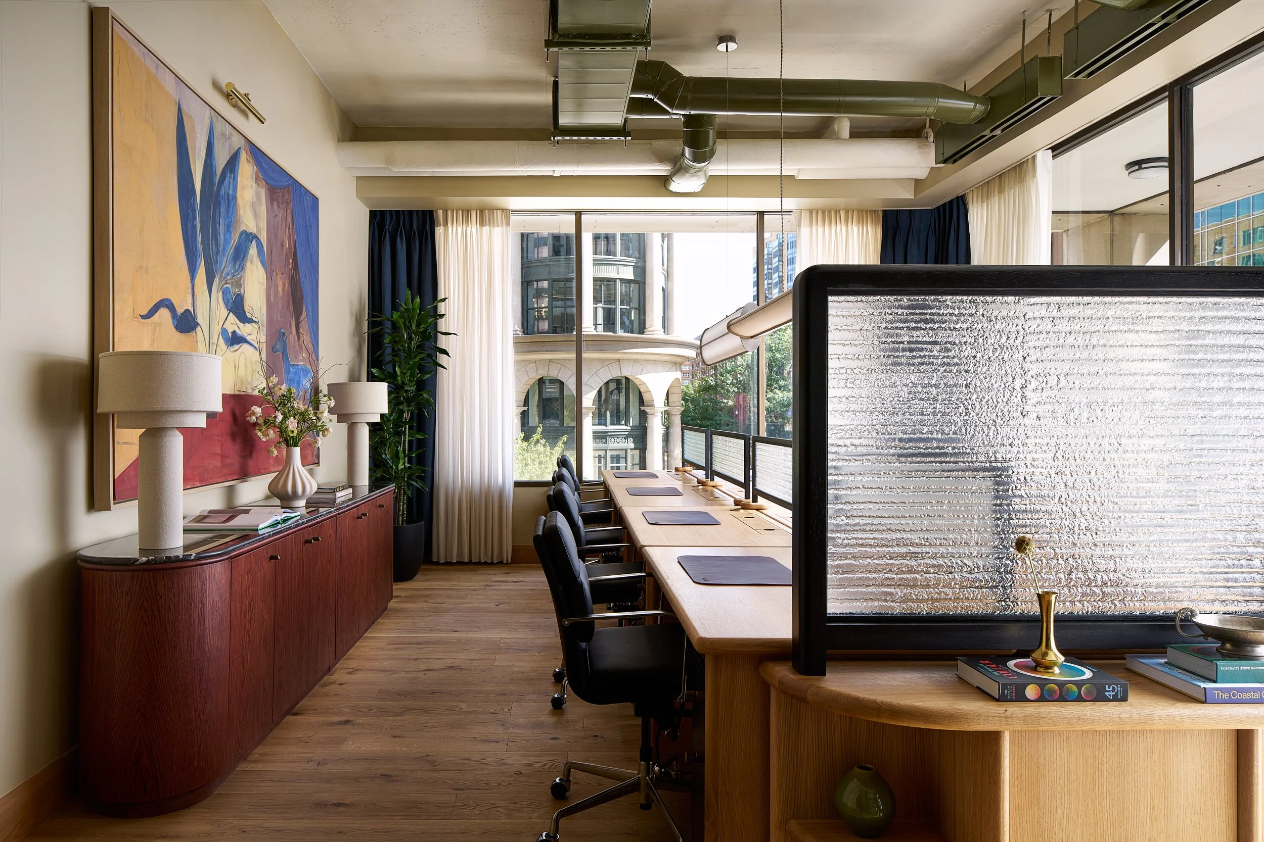 Shared desks and workstations at The Malin DC with wood desks, a red credenza, and a colorful painting overlooking the DC skyline.