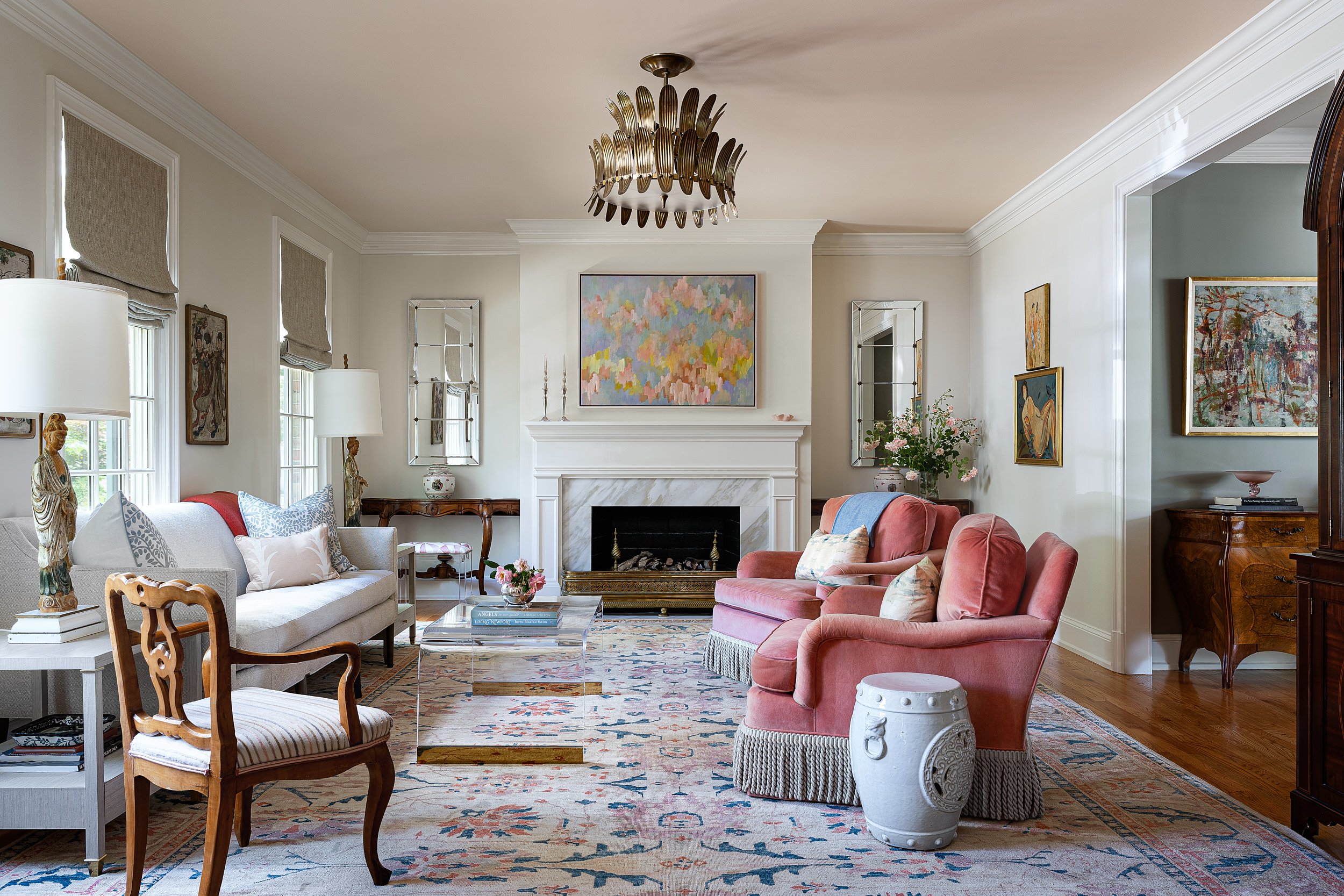 Living room with coral swivel chairs, a gold sunburst chandelier, and a colorful vintage rug, interior design photography in the DMV area