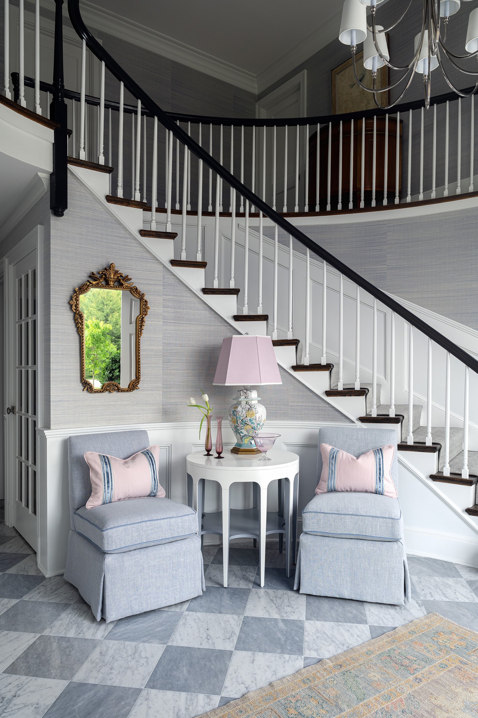 Foyer seating area beneath a curved staircase with checkerboard marble flooring, interior design photography in Northern Virginia