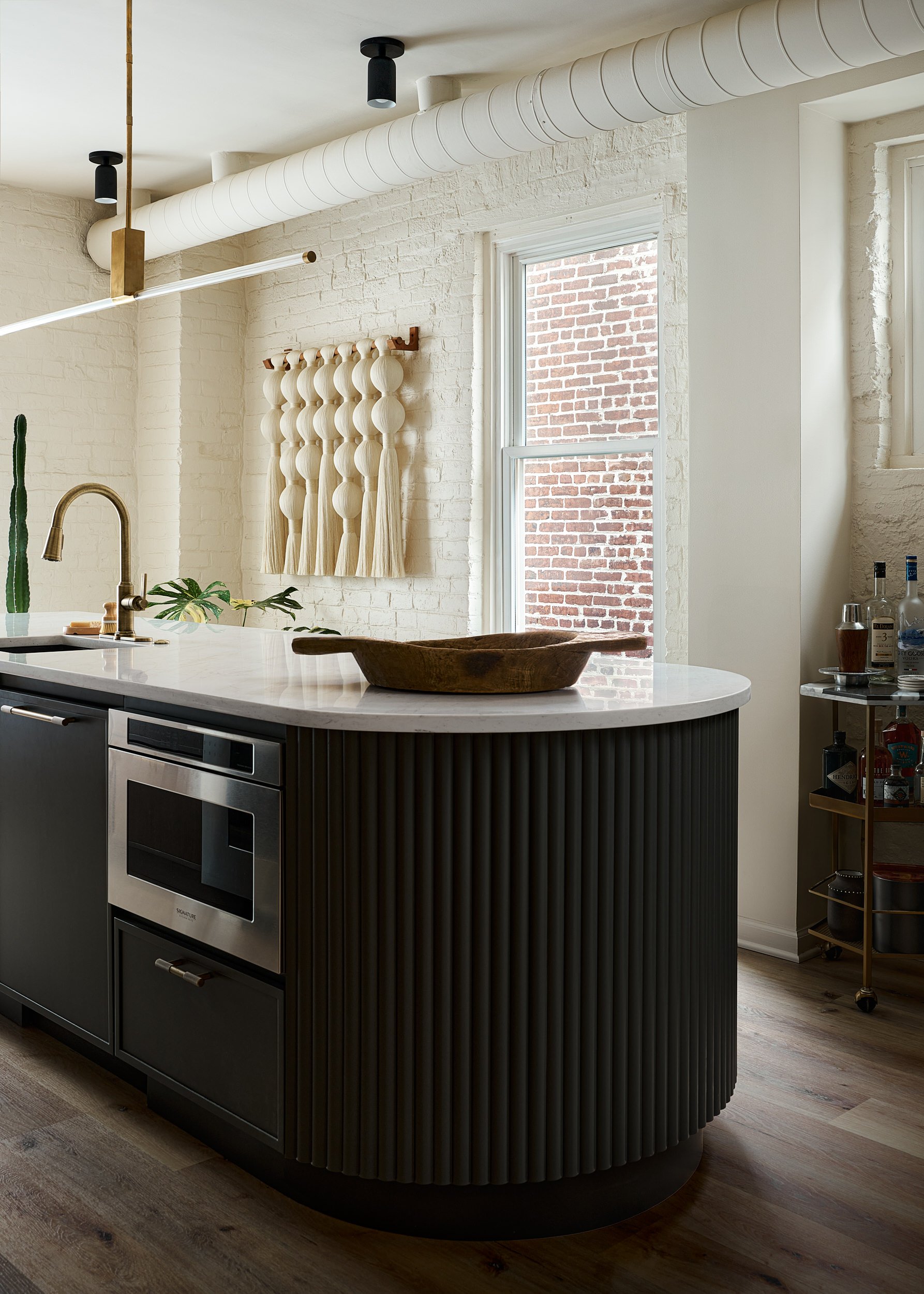Kitchen with a black waterfall island and exposed brick accent wall, interior design photography in Washington, DC
