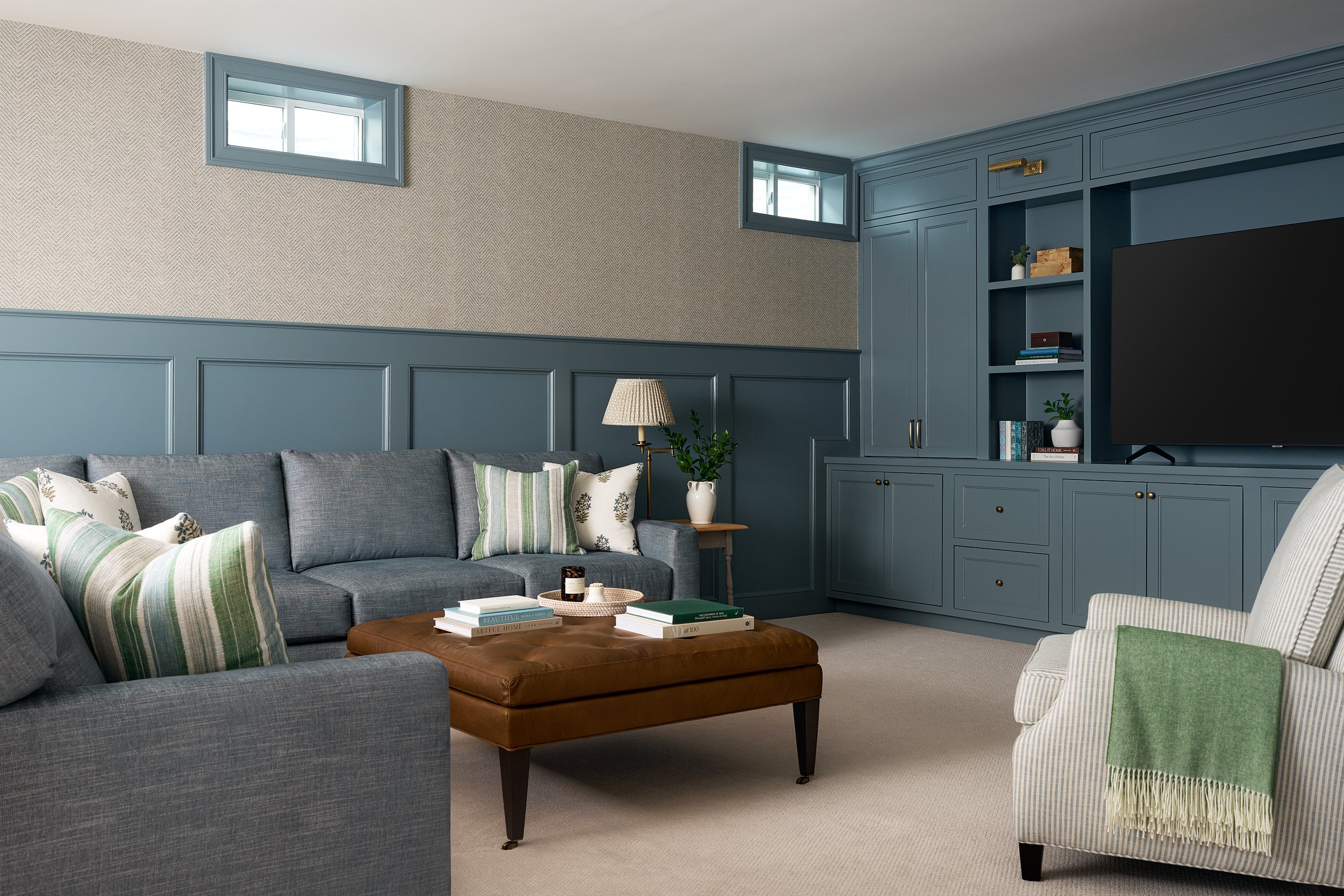 Basement family room with blue built-in media cabinetry and a leather ottoman, interior design photography in Washington, DC