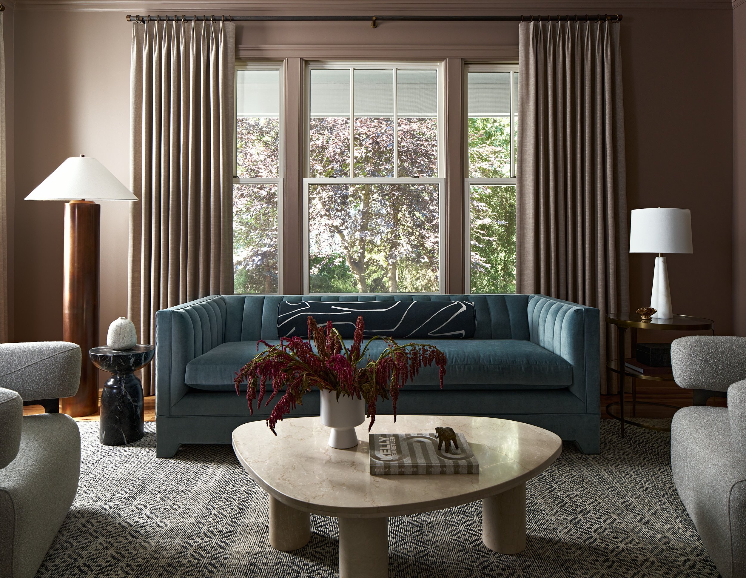 Living room with a teal channel-tufted sofa, dusty mauve walls, and a tri-leg marble coffee table, interior design photography in Northern Virginia