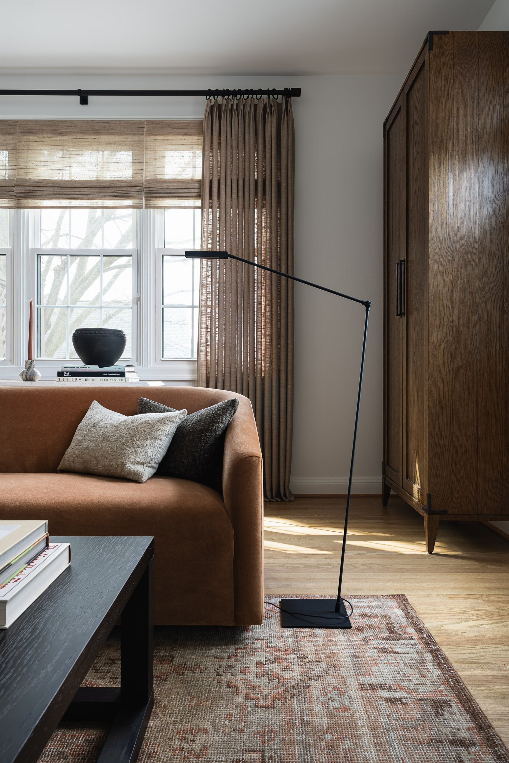 Living room with a rust velvet sofa, woven wood shades, and a walnut wardrobe, interior design photography in Maryland