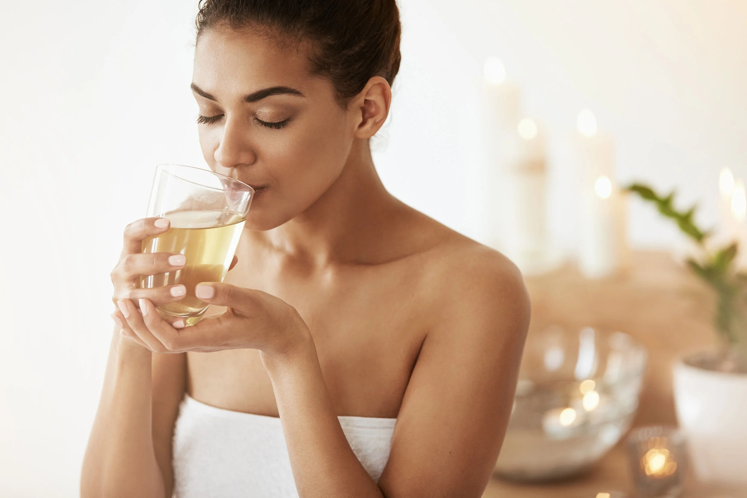 Attractive african girl drinking green tea resting in spa salon. Closed eyes.