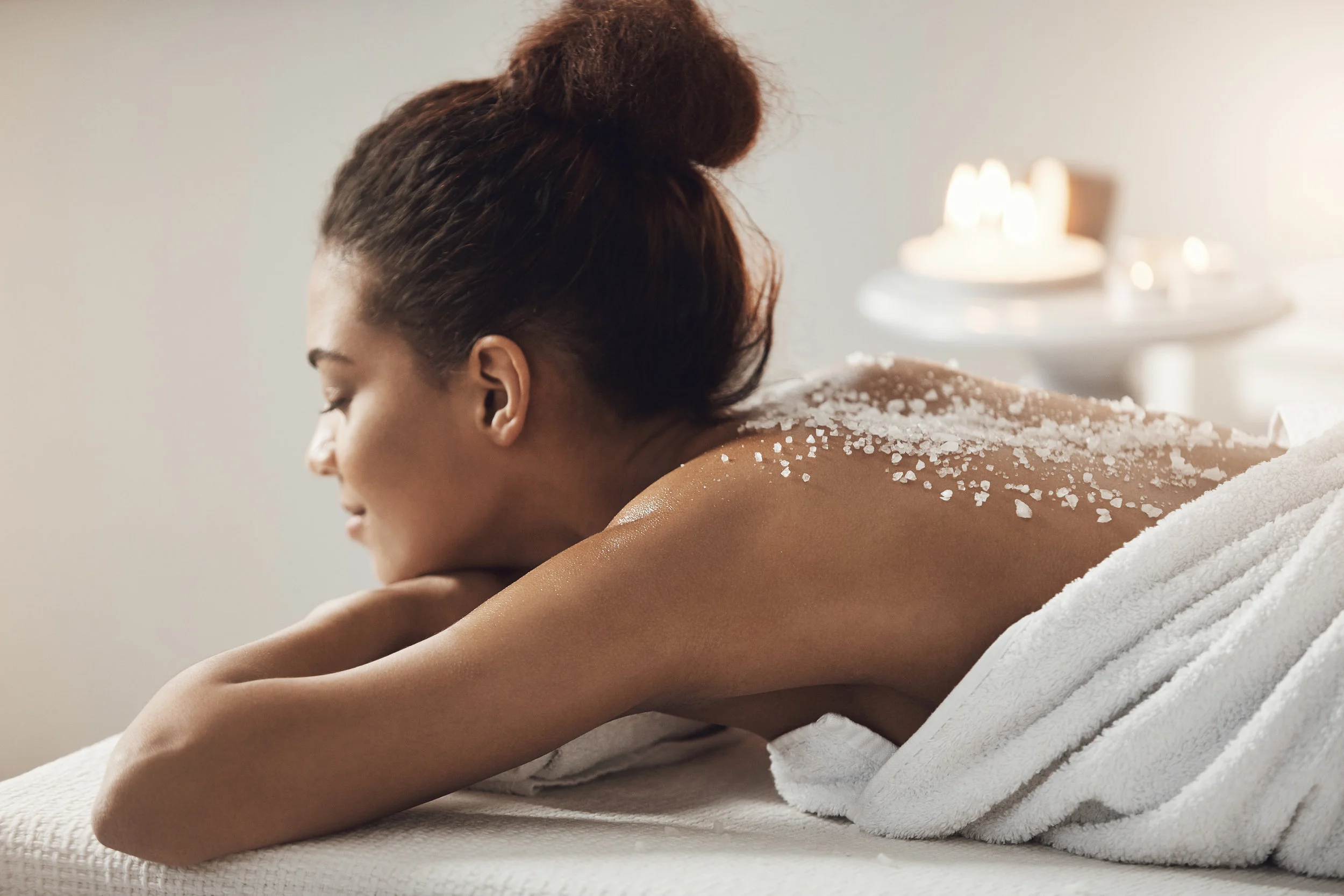 Copy of Beautiful african girl resting relaxing with sea salt on back in spa salon.