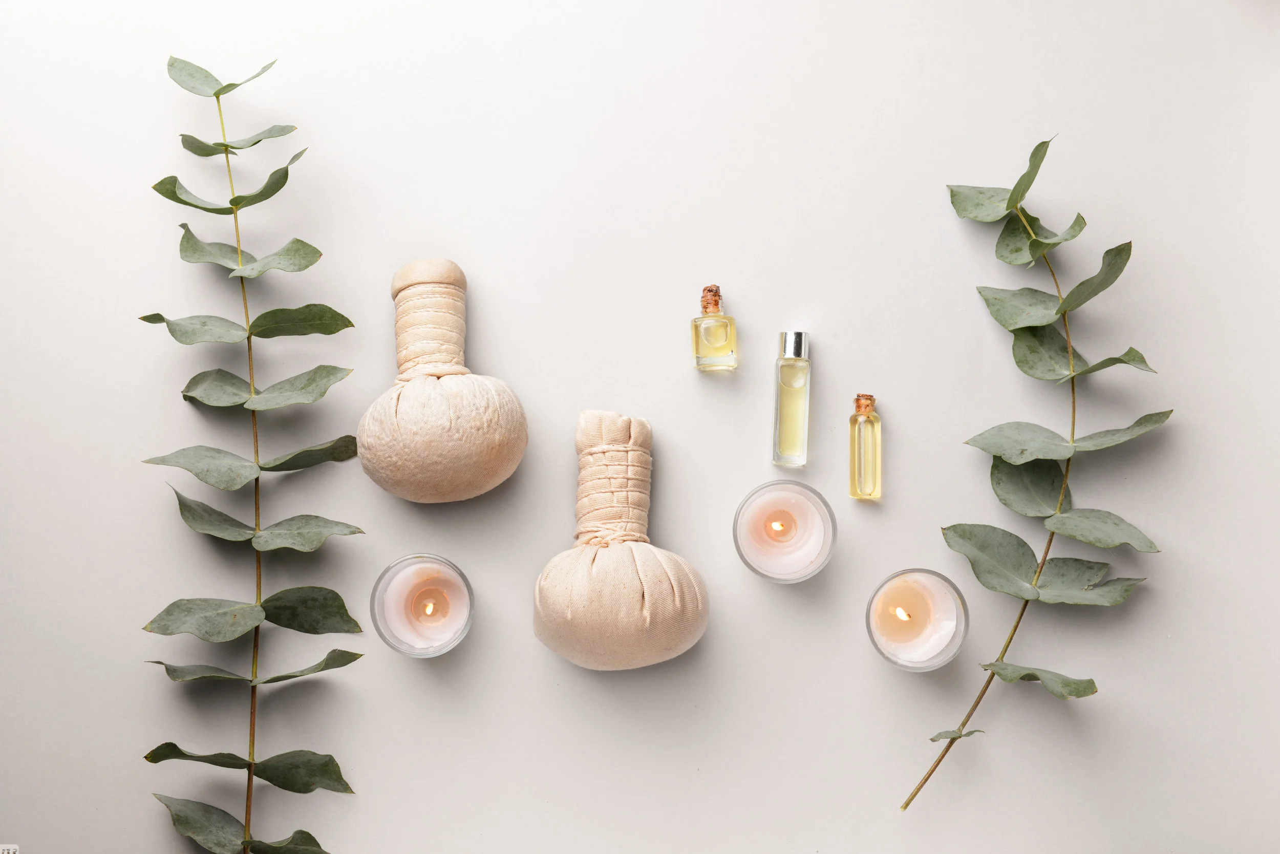 Spa composition with herbal bags, candles and essential oil on light background