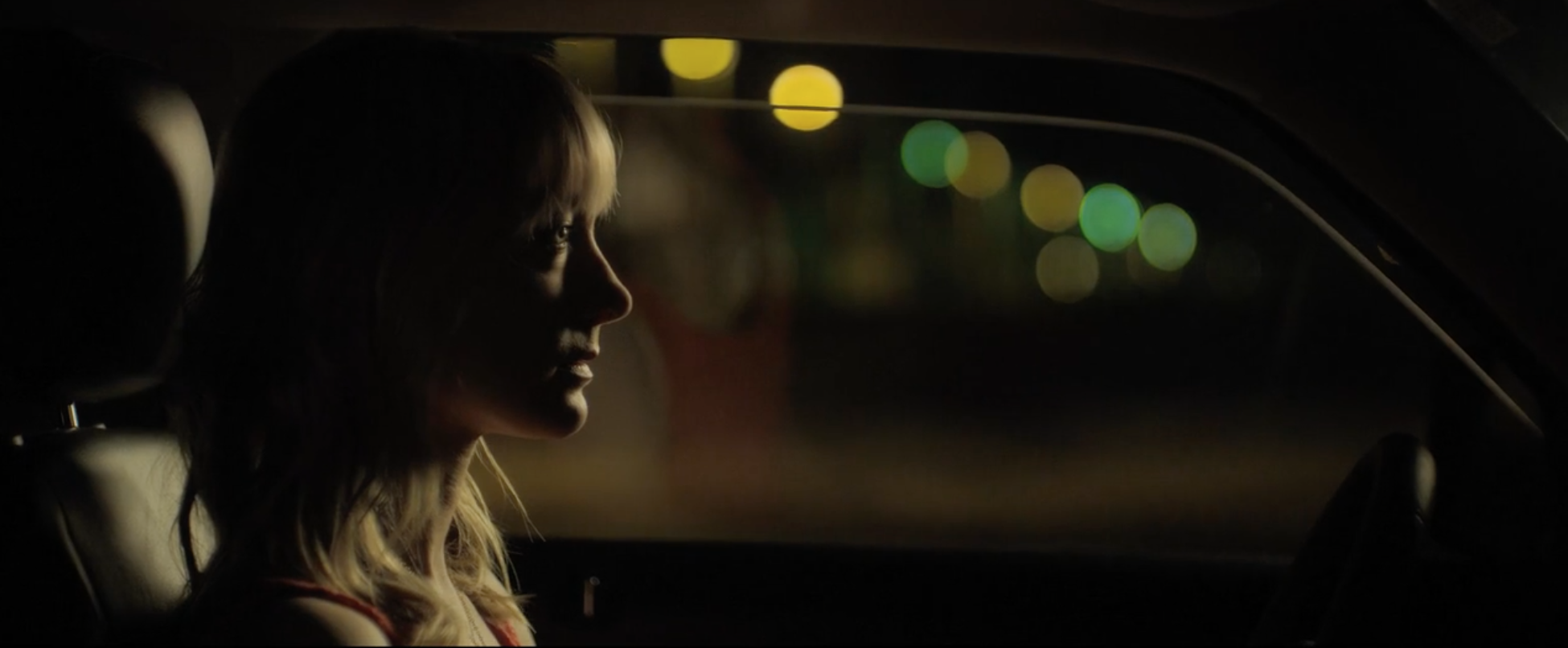 A profile shot of a woman sitting in her car, looking distraught.