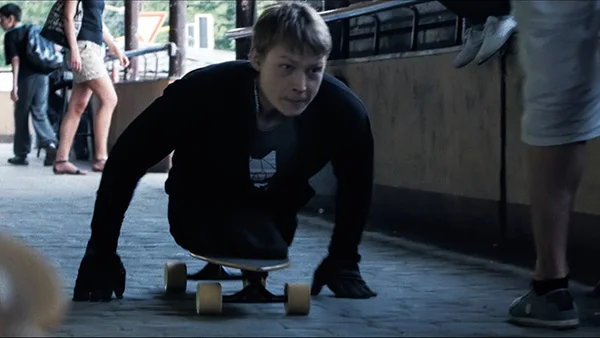 A young man rolls with his torso on a skateboard and pushes himself along a cobblestoned street.