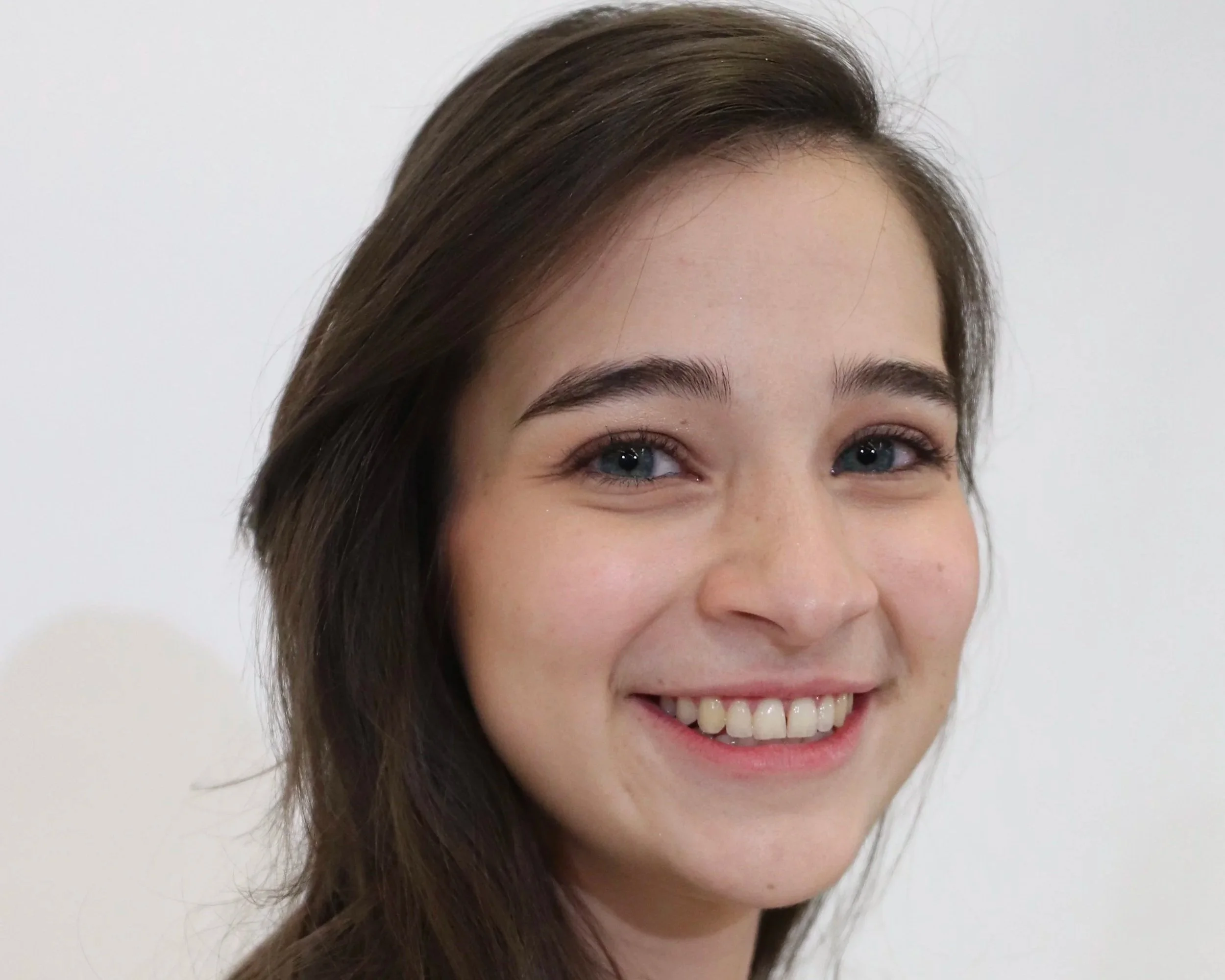 Close-up of a woman's face, showing her smiling with blue eyes and brown hair, against a plain white background.