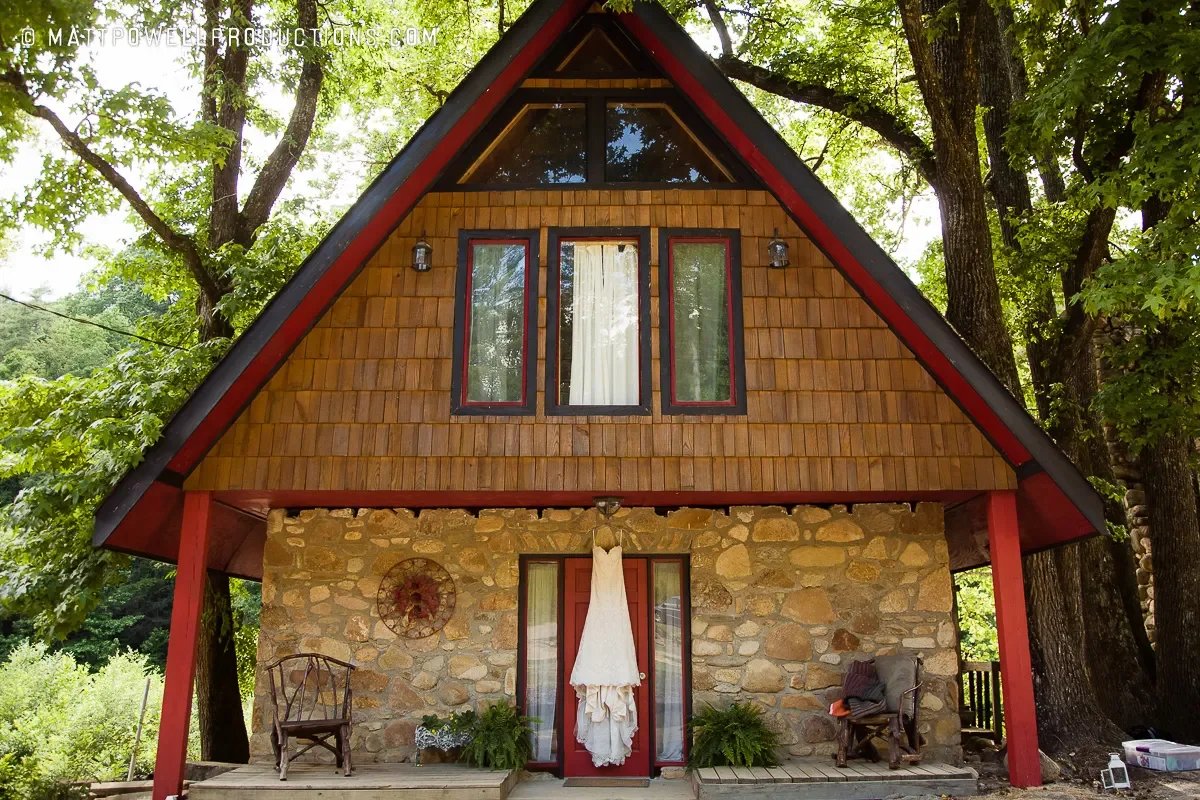 Wedding dress hanging on the porch of a stone cabin under tall trees