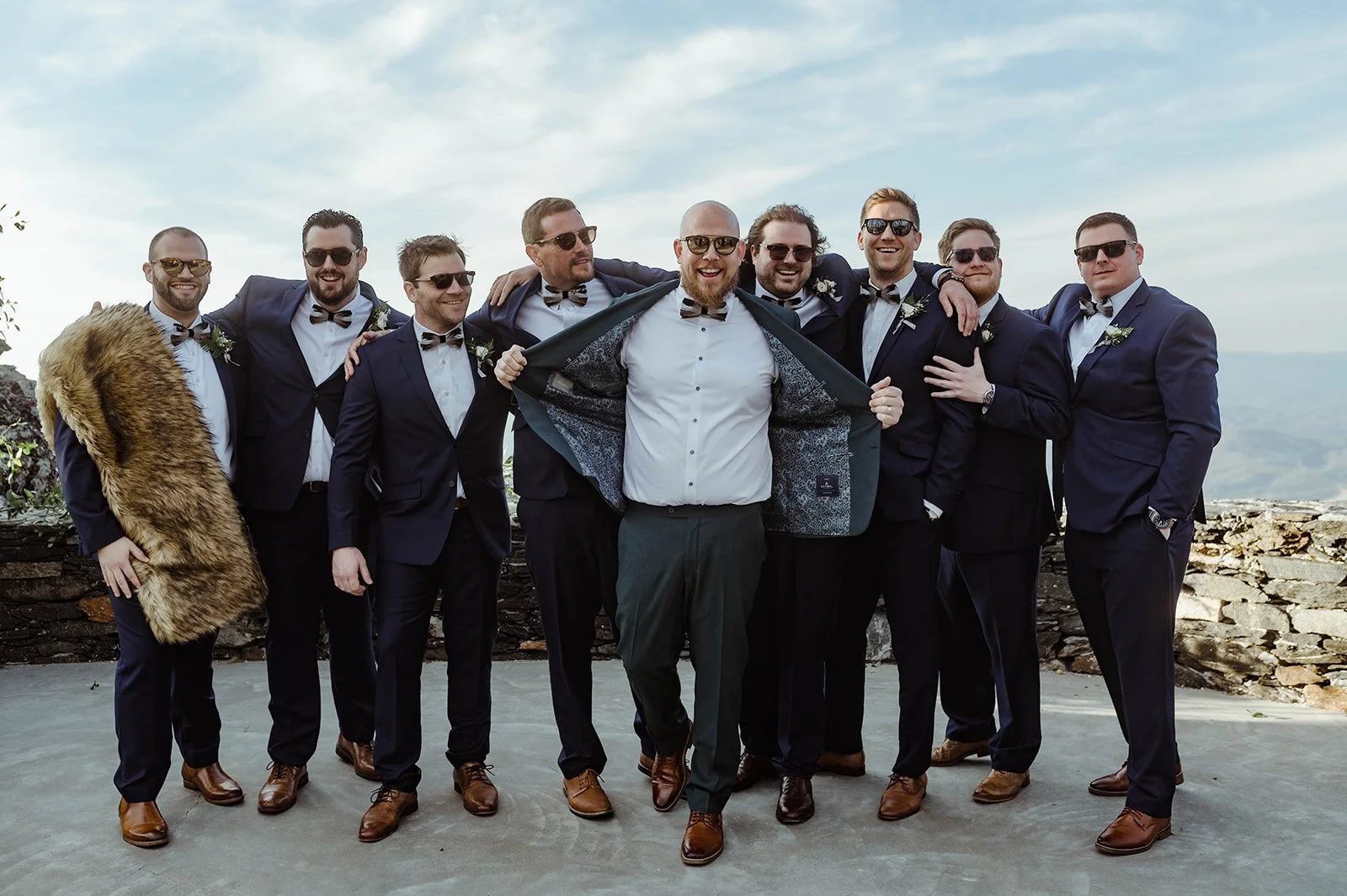 Groomsmen posing together in navy suits on an outdoor terrace, smiling and celebrating