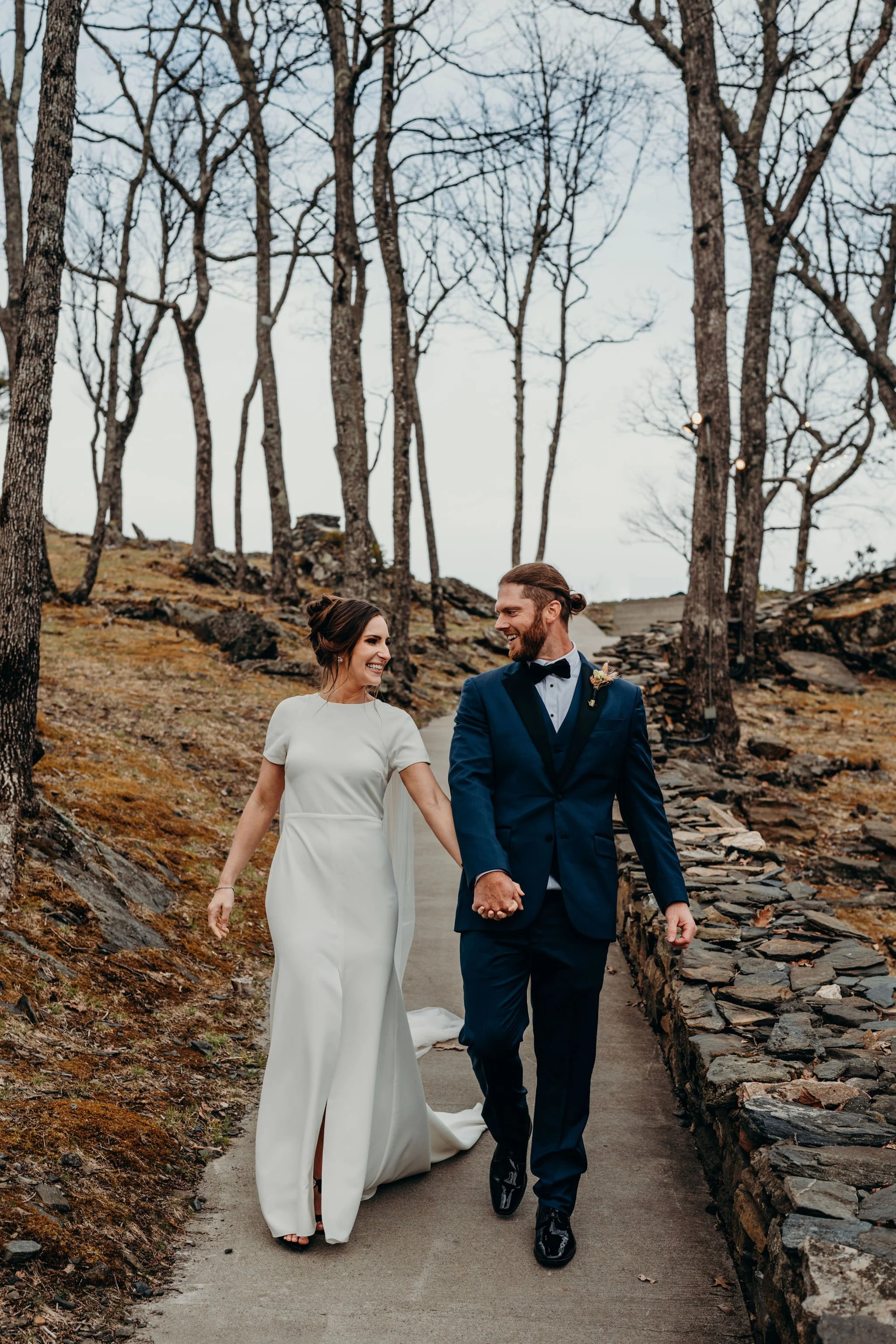Bride and groom walking hand in hand along a path at a mountain venue after the ceremony.