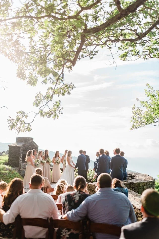 Mountain wedding ceremony seen from the guests’ perspective under leafy trees.