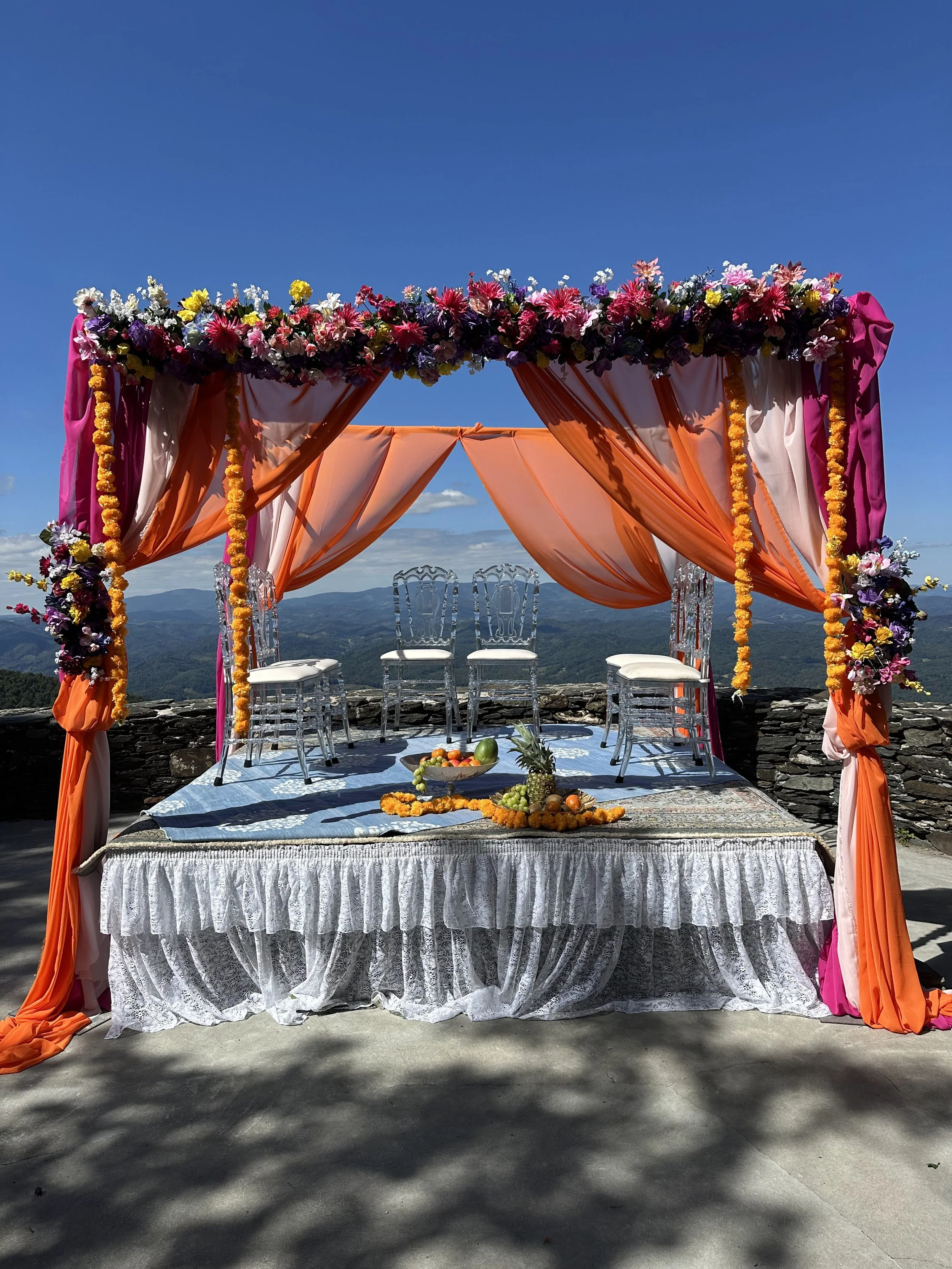 Colorful Indian wedding mandap with pink and orange draping and floral decor on a mountain overlook