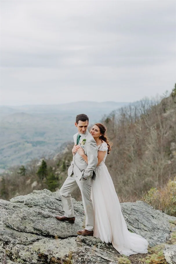 Bride and groom posing on a rocky mountain overlook with a sweeping valley view