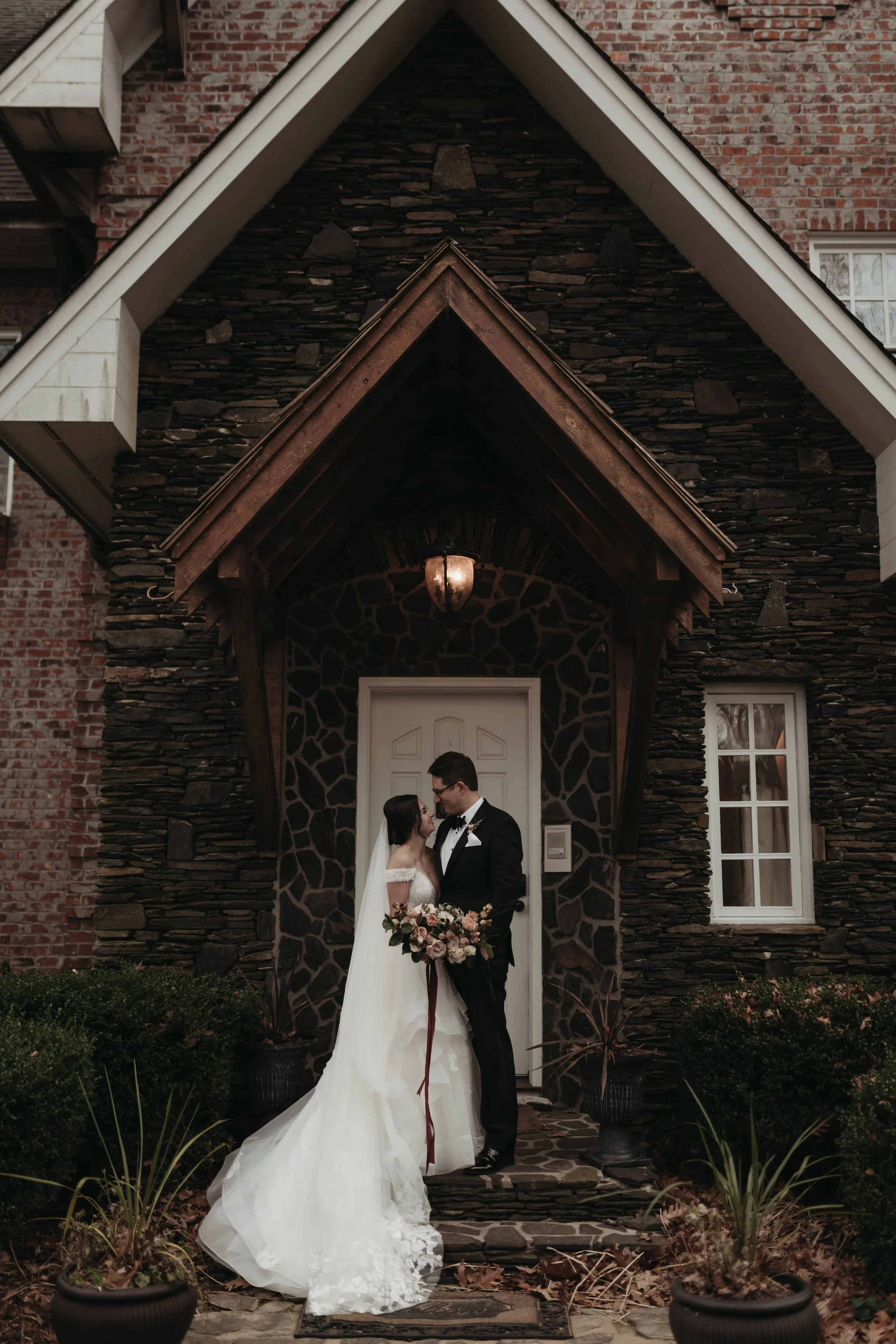 Bride and groom standing together in a stone chapel doorway holding a bouquet.