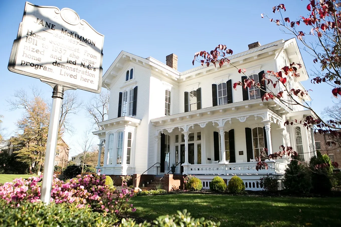 Historic white Victorian home exterior with a historical marker sign in the foreground