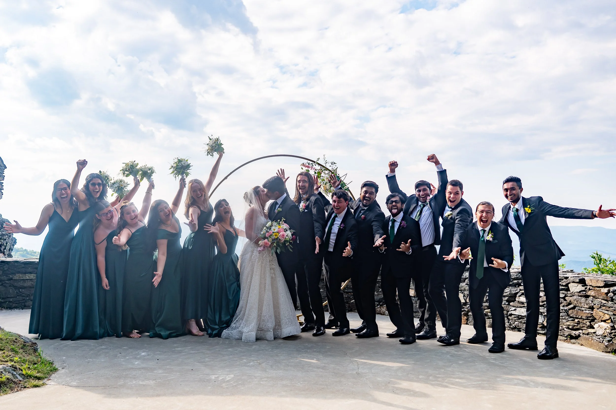 Wedding party cheering with bride and groom at a scenic mountain overlook ceremony location.