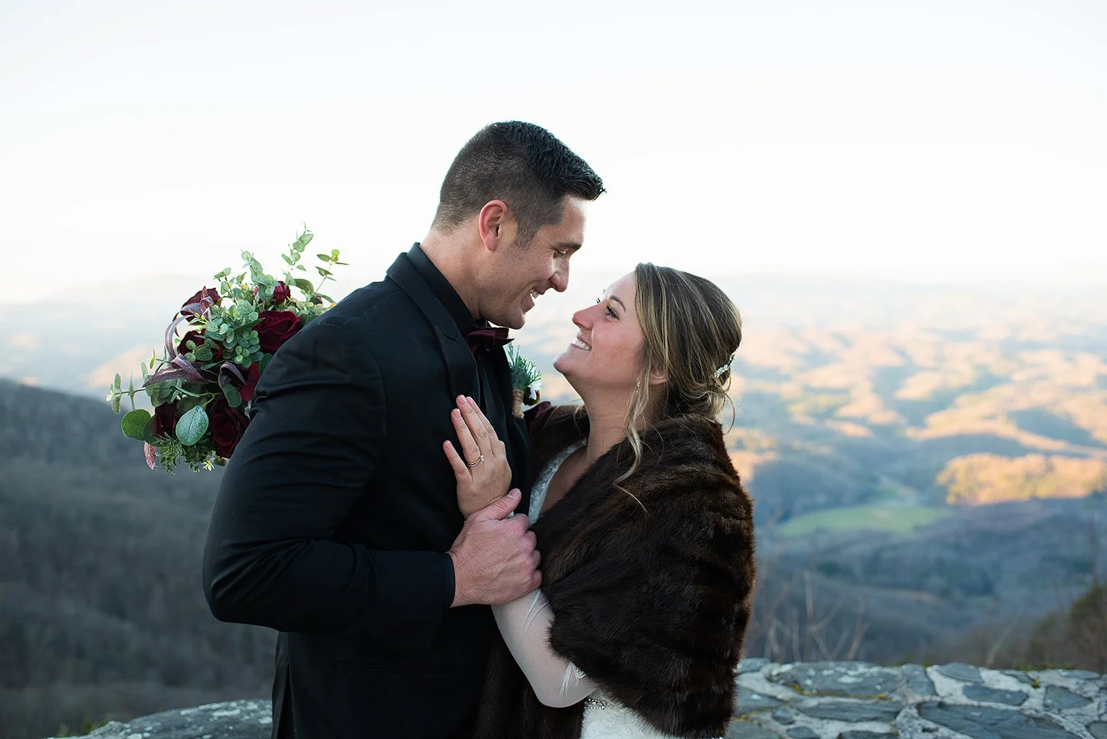Closeup of the couple smiling at each other, bride wearing a fur wrap during outdoor portraits.
