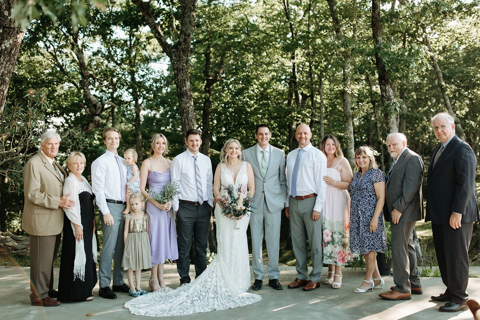 Bride and groom posing with family members for a wedding portrait in a wooded outdoor setting.
